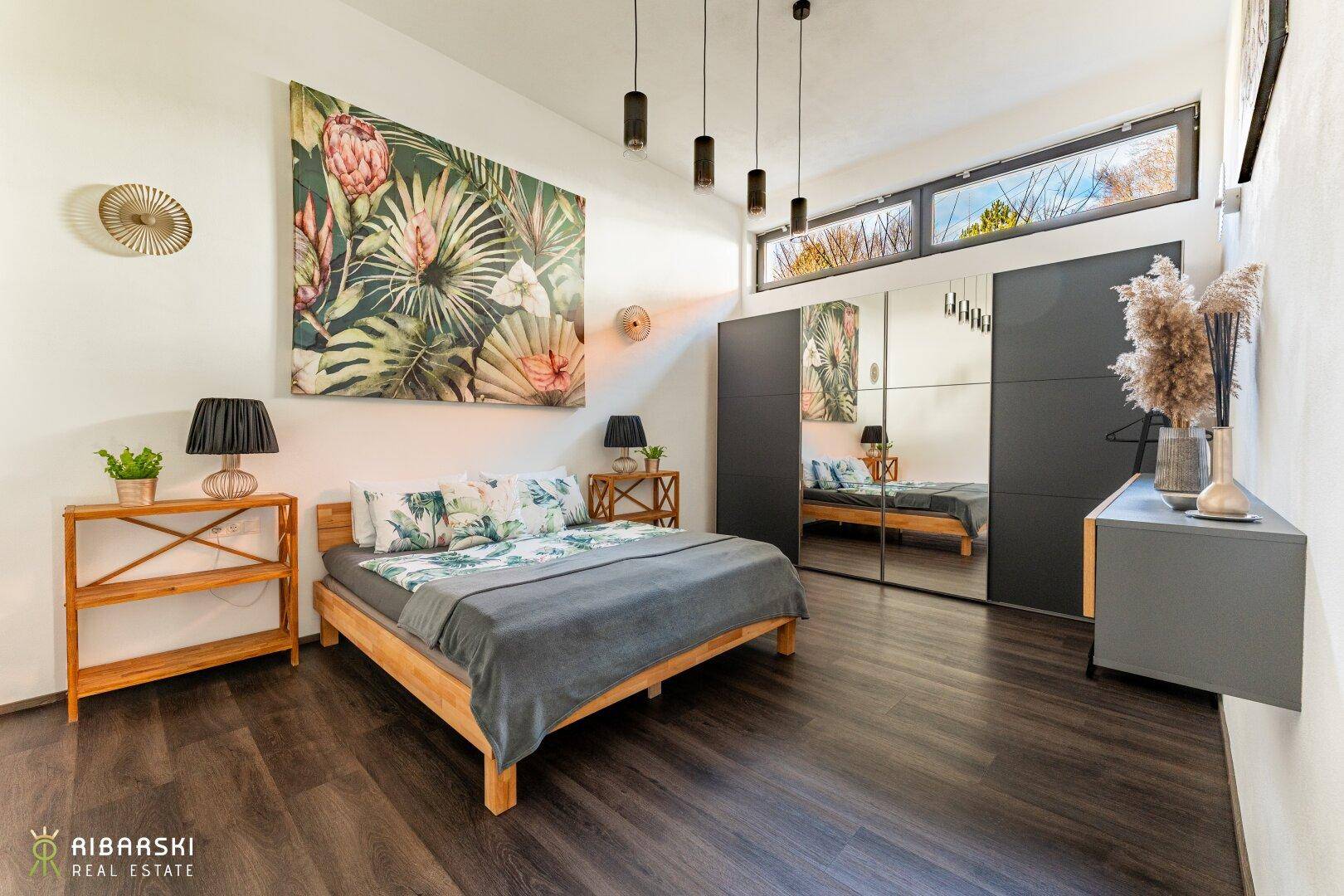 Helles Schlafzimmer mit Holzbett, großem Spiegelkleiderschrank und floraler Wanddekoration.