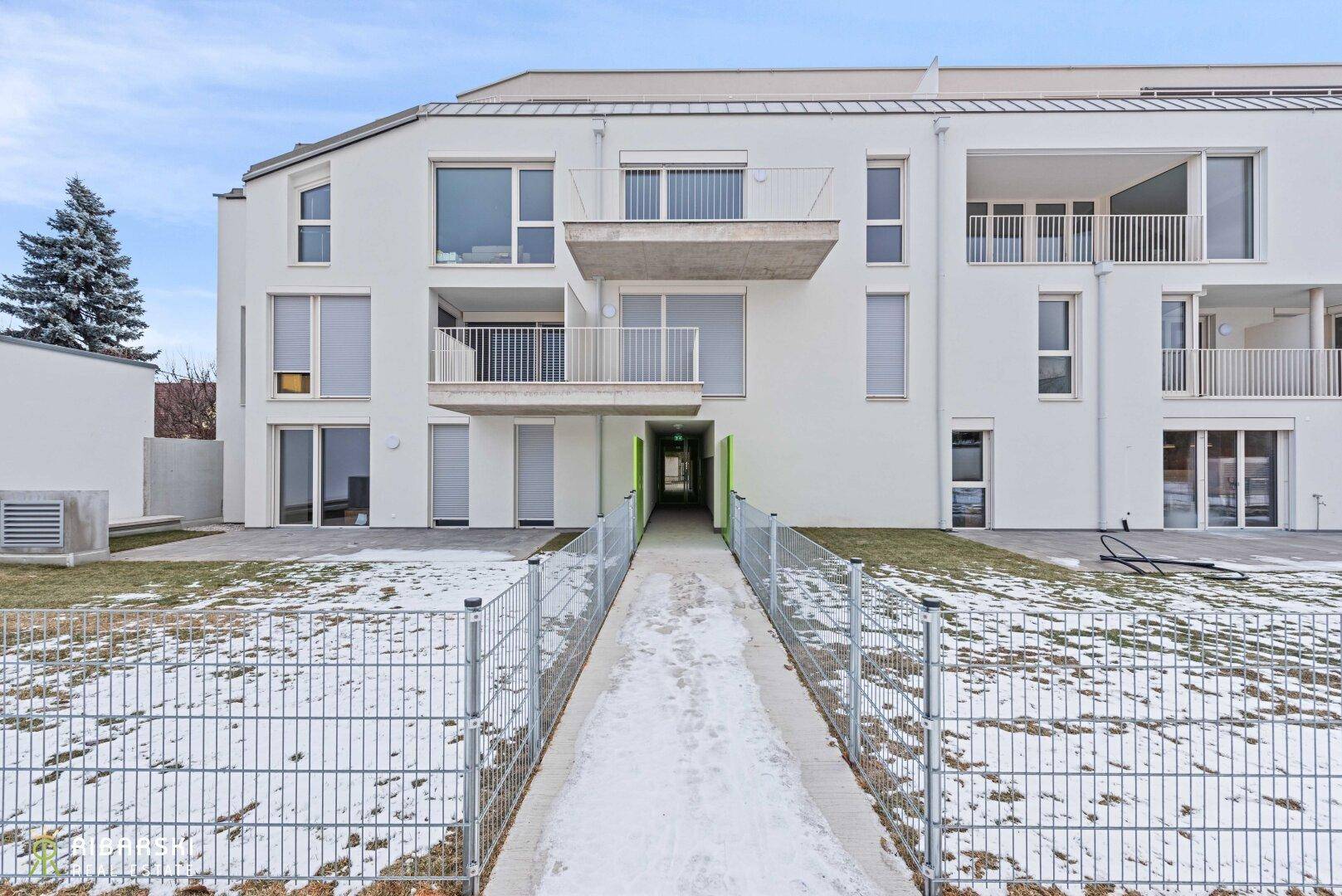 Moderne Wohnanlage mit weißer Fassade, Balkonen und einem verschneiten Zugangsweg.