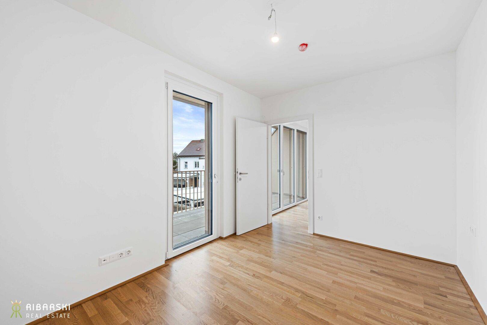 Helles Schlafzimmer mit Holzboden und direktem Zugang zu einem kleinen Balkon.