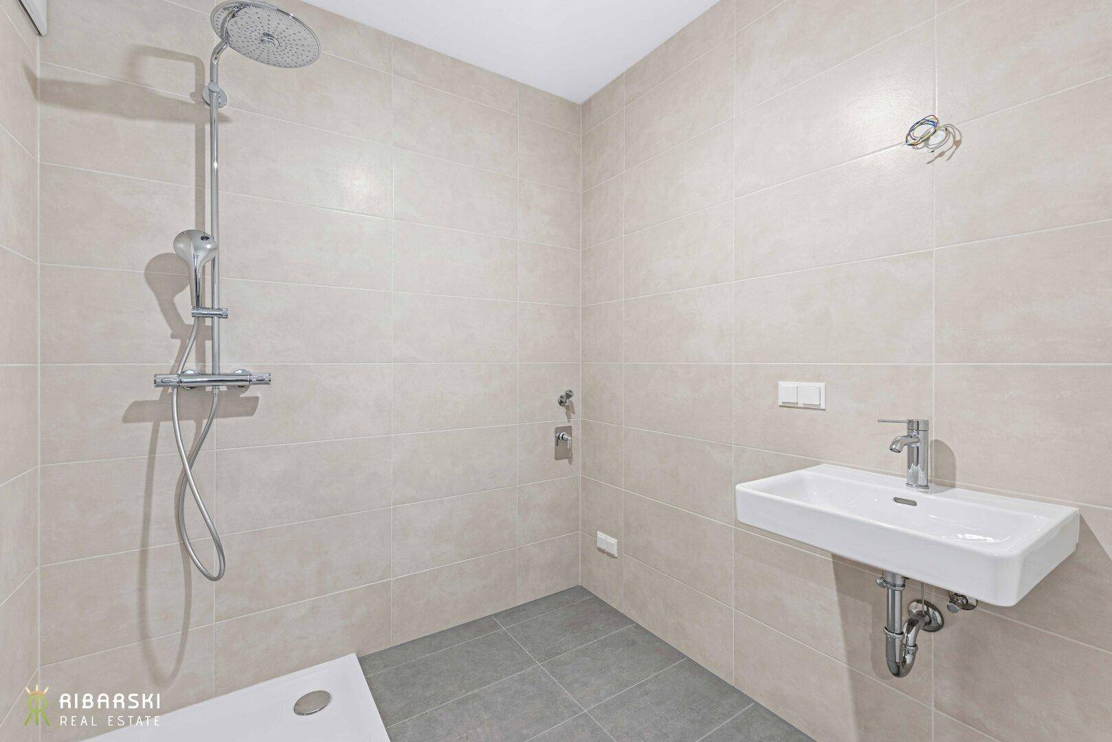 Modernes Badezimmer mit beigefarbenen Fliesen, ebenerdiger Dusche und Wandwaschbecken.