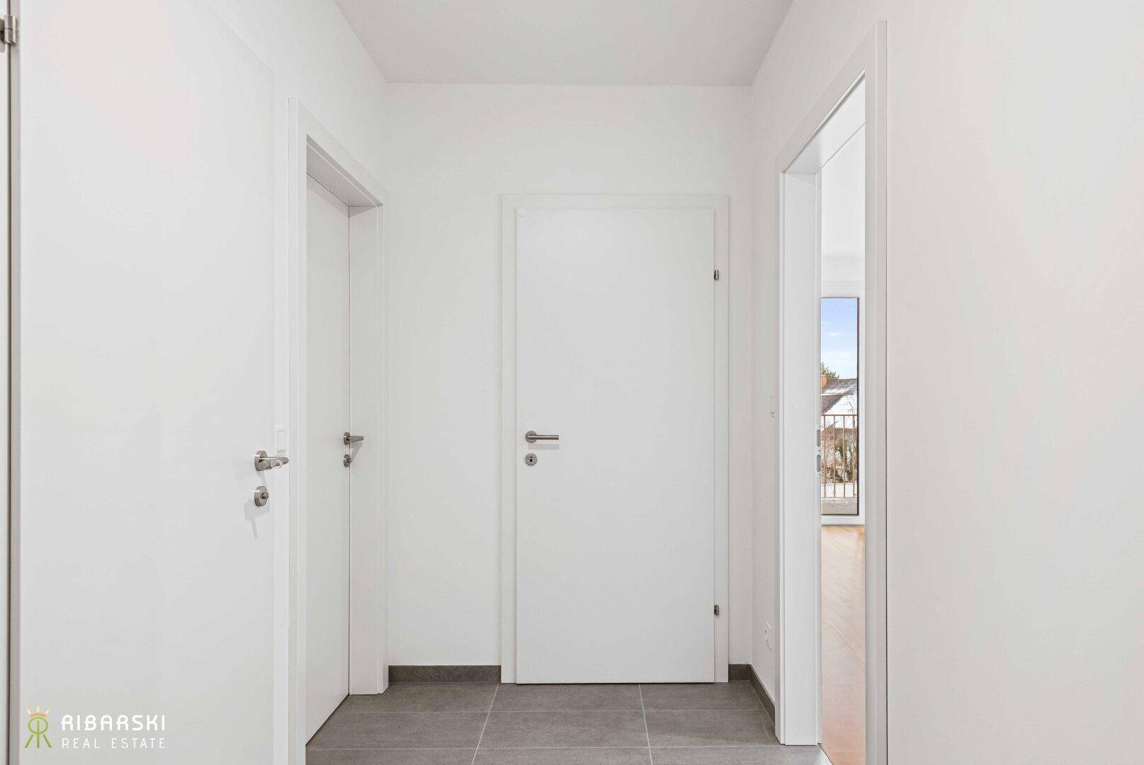 Heller Flur mit Fliesenboden und mehreren Türen, der verschiedene Räume verbindet.