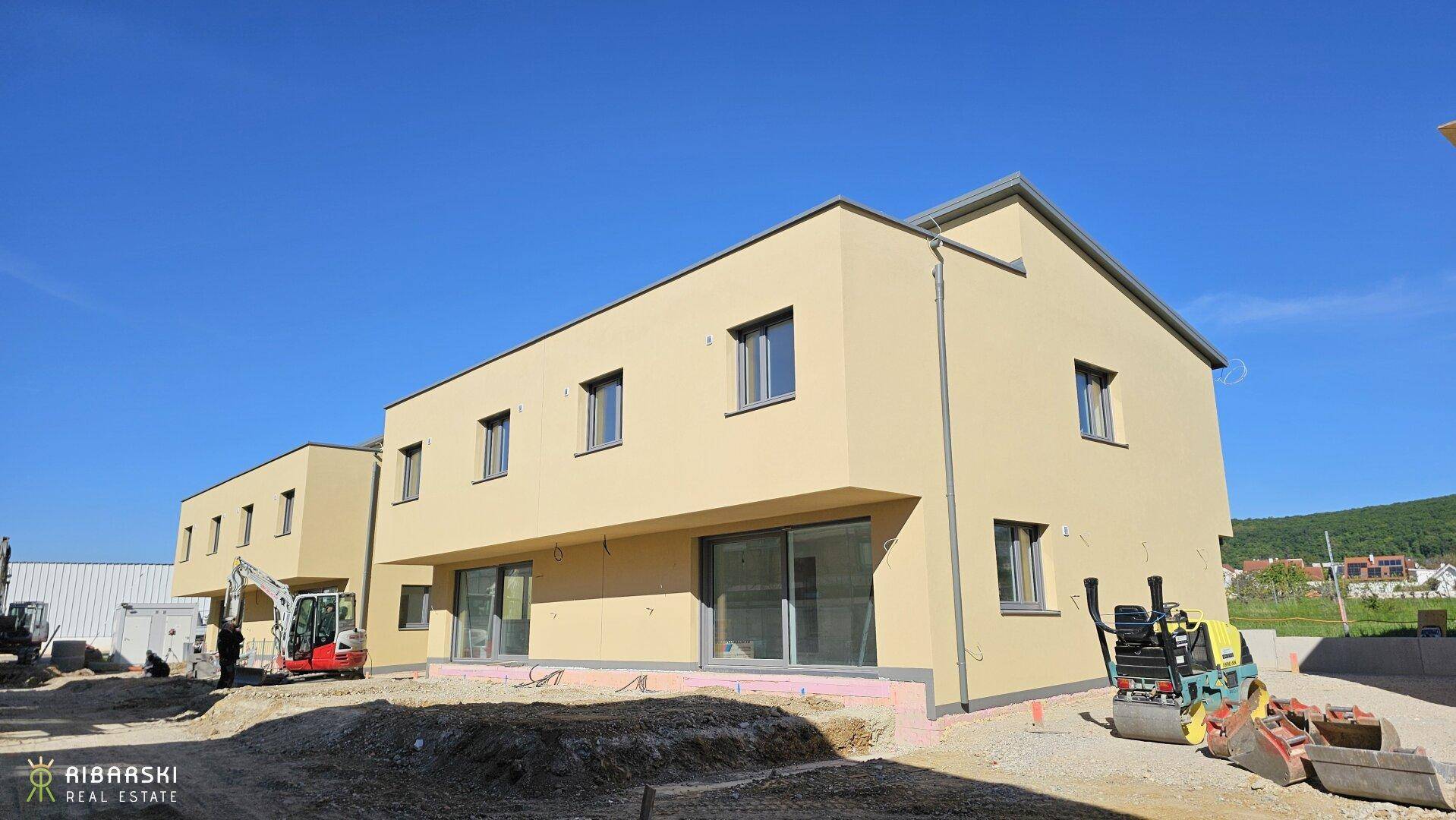 Neubau eines modernen Reihenhauses mit heller Fassade und Baustelle im Vordergrund.