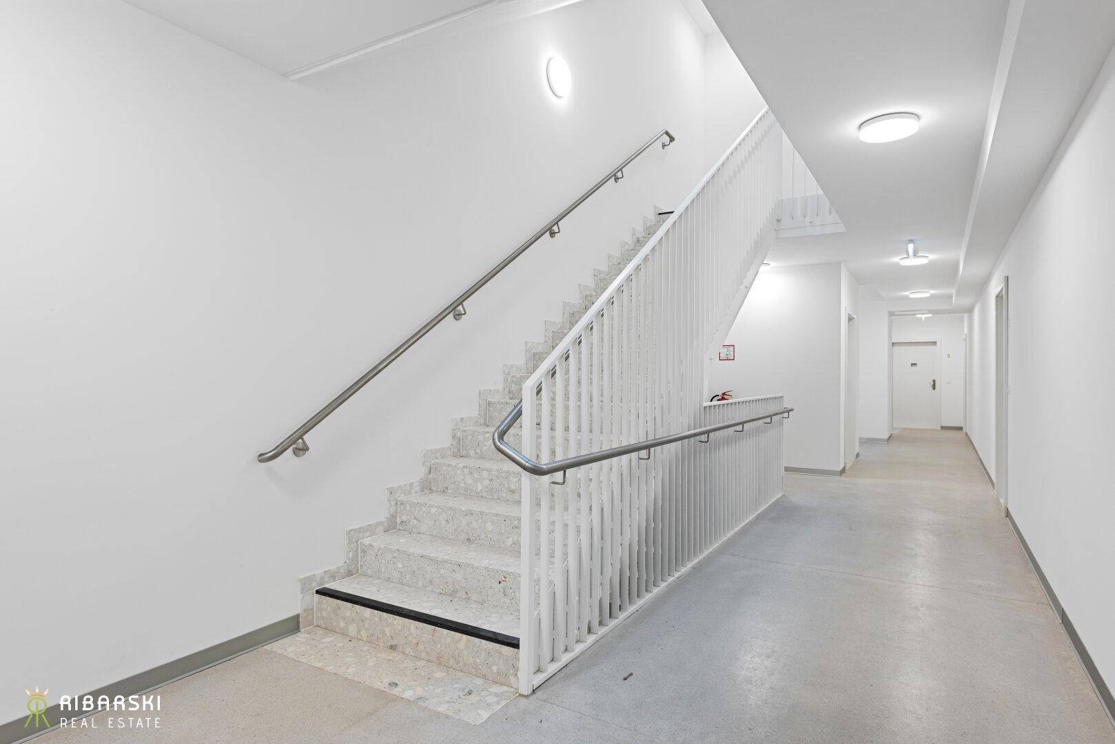 Modernes Treppenhaus mit hellem Marmorboden und schlichten Geländern in einem Mehrfamilienhaus.
