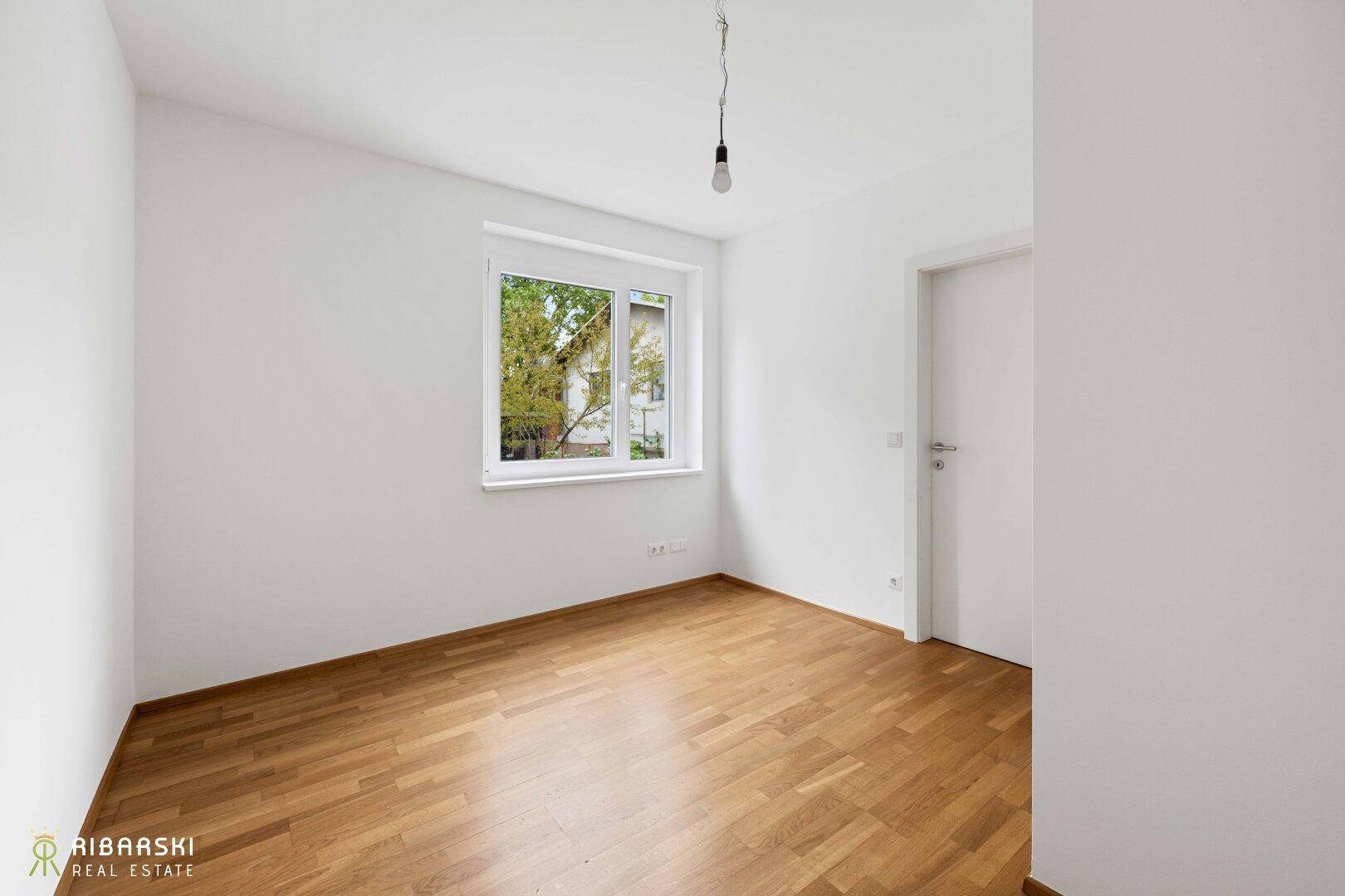 Ruhiges Schlafzimmer mit hellem Parkettboden und Fenster mit Blick ins Grüne.