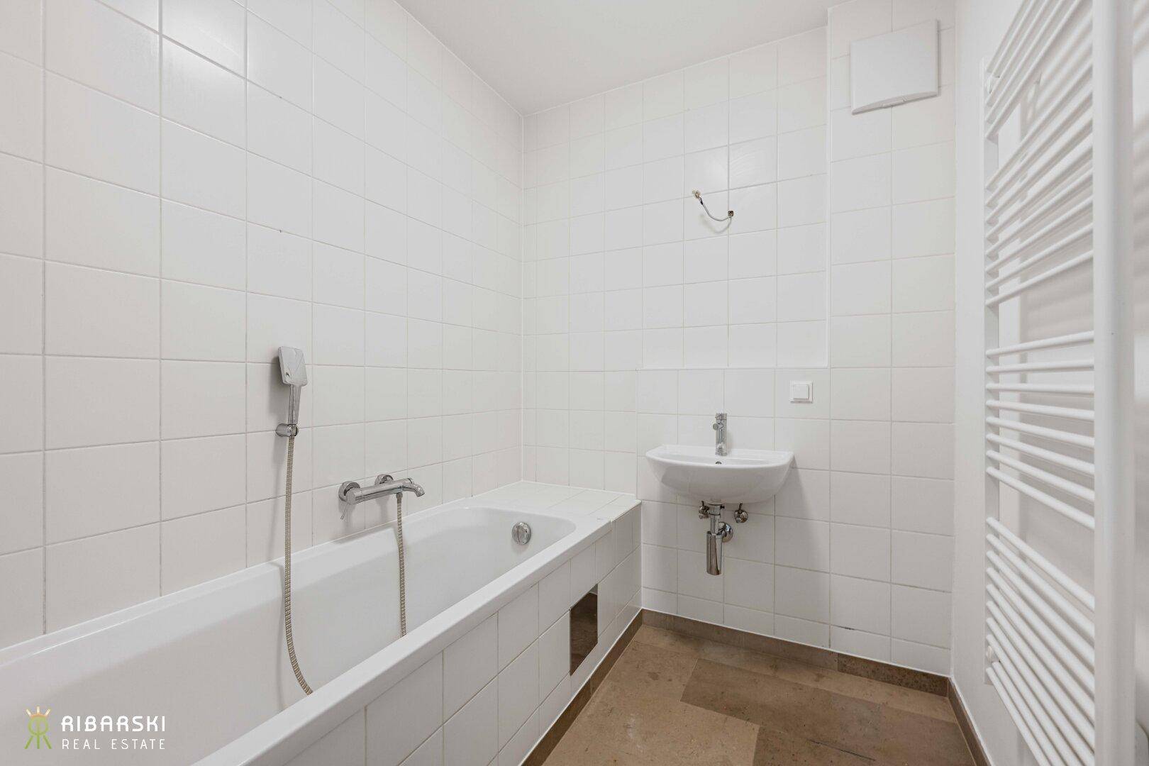 Helles Badezimmer mit Badewanne, Waschbecken und beheiztem Handtuchhalter.