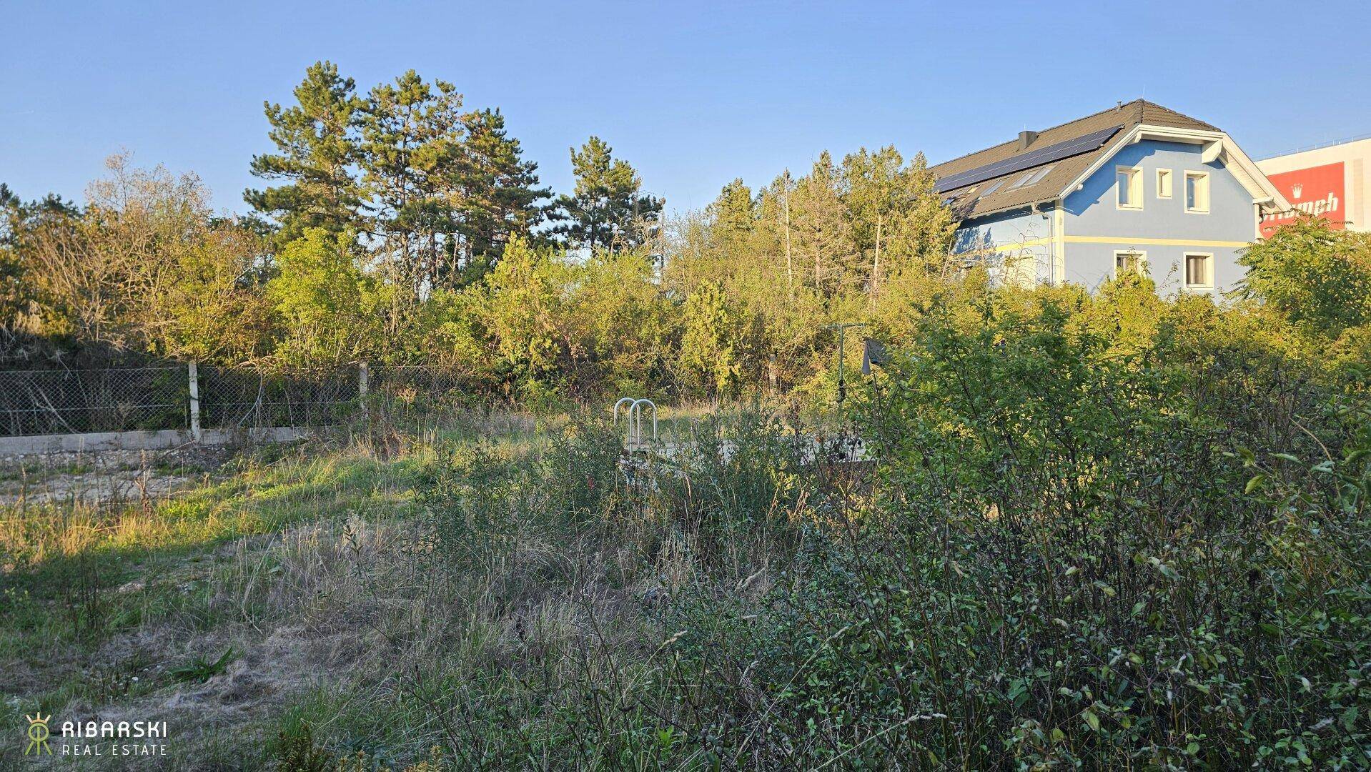 Großes, grünes Grundstück mit einem abgedeckten Pool und einem Haus mit Solaranlage im Hintergrund.
