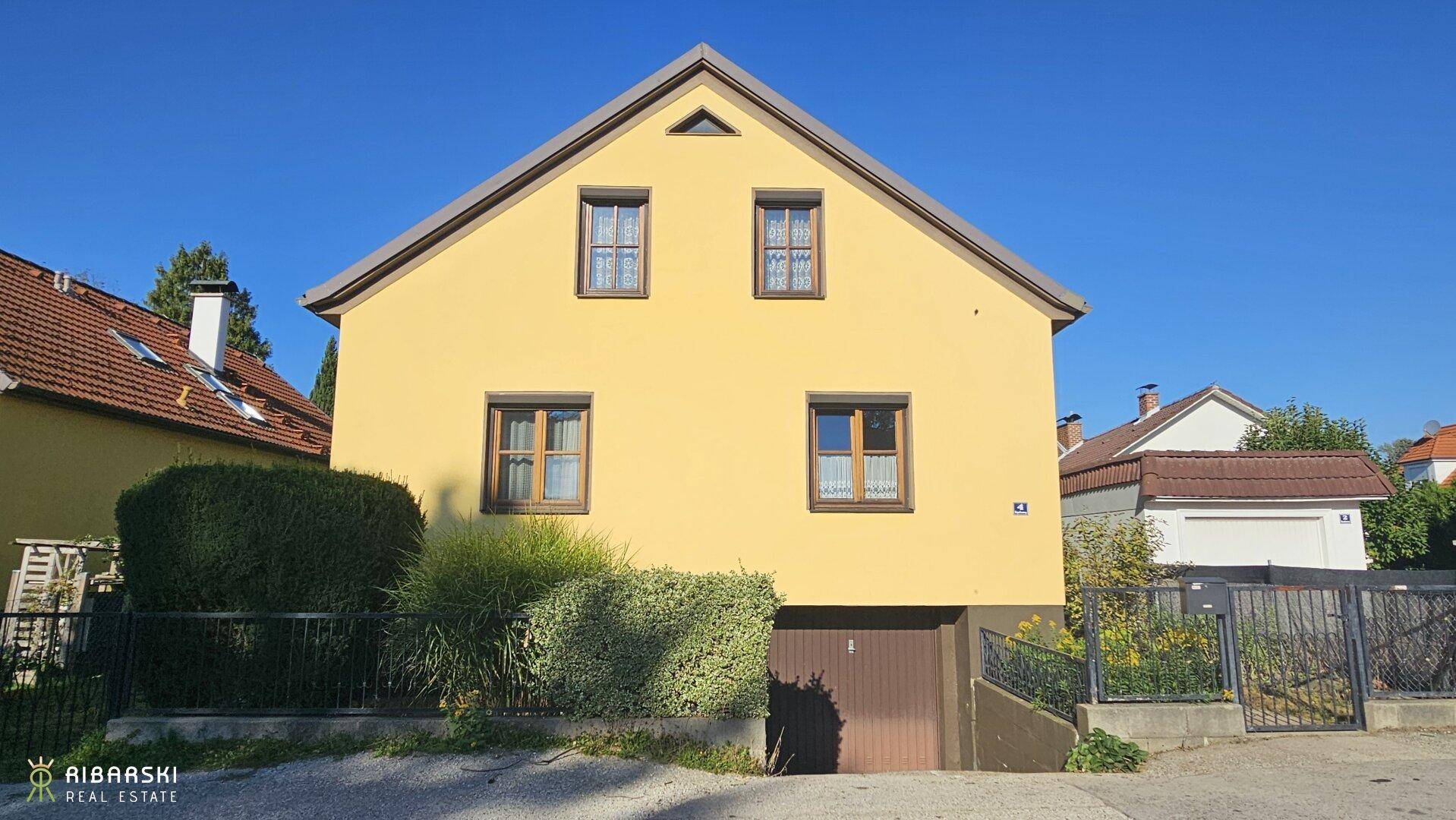 Vorderansicht des gelben Einfamilienhauses mit integrierter Garage und Rollläden an den Fenstern.