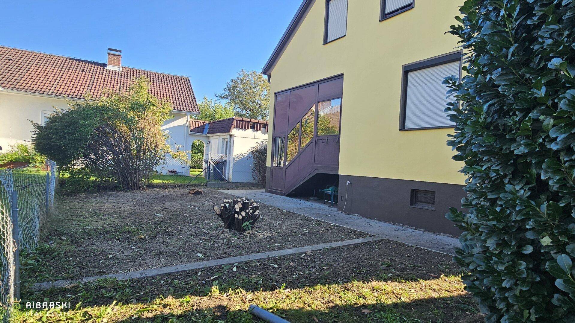 Gartenbereich hinter dem Haus mit Rasenfläche und Zugang zum verglasten Anbau.