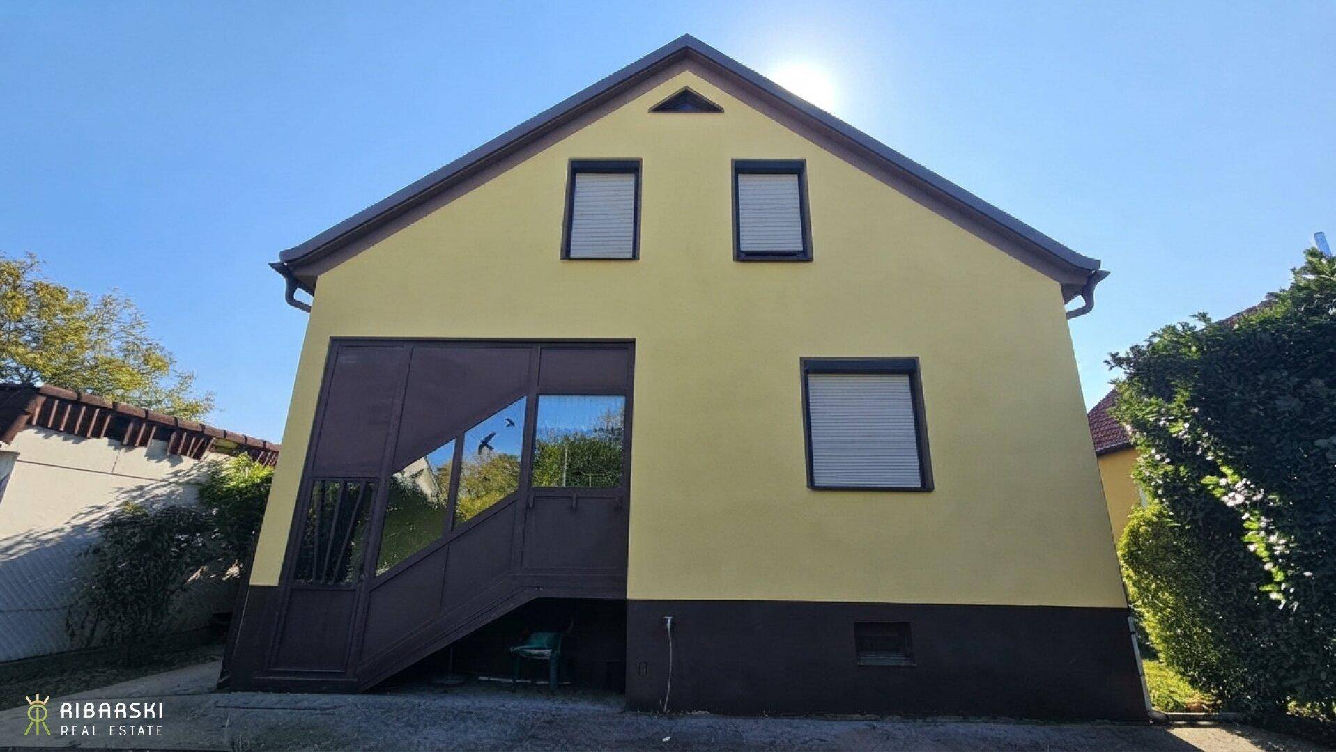 Rückansicht des Hauses mit verglastem Anbau und Rollläden an den Fenstern.