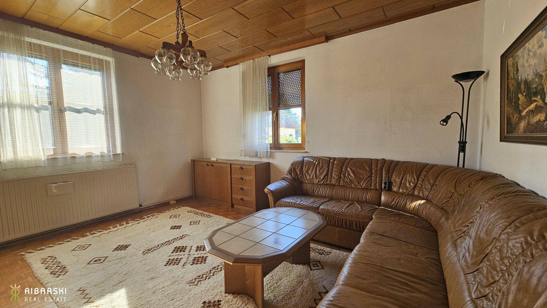 Geräumiges Wohnzimmer mit Ledersofa, Holztisch und Teppich, unter einer Holzdecke.