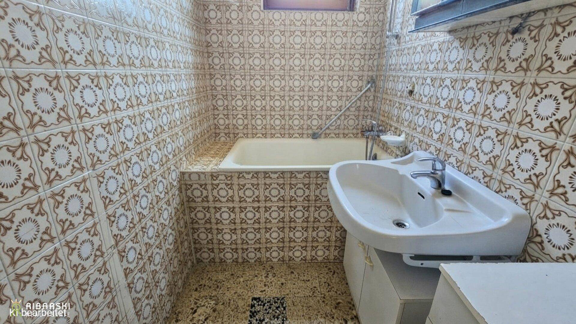 Badezimmer mit Badewanne, Waschbecken und auffälligen gemusterten Fliesen im Retro-Stil.