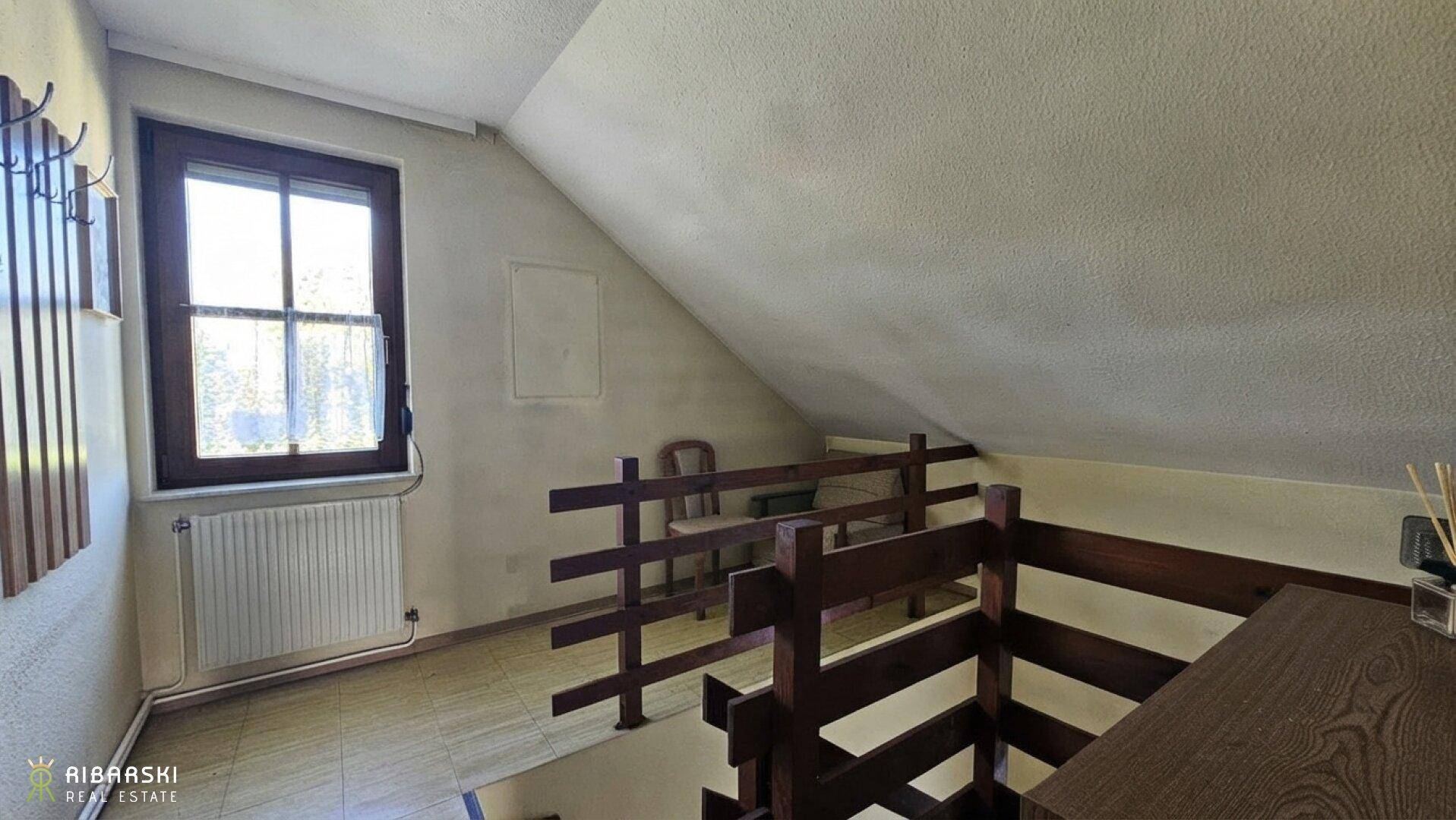 Heller Flur im Dachgeschoss mit Holzgeländer und Fenster, das viel Tageslicht hereinlässt.