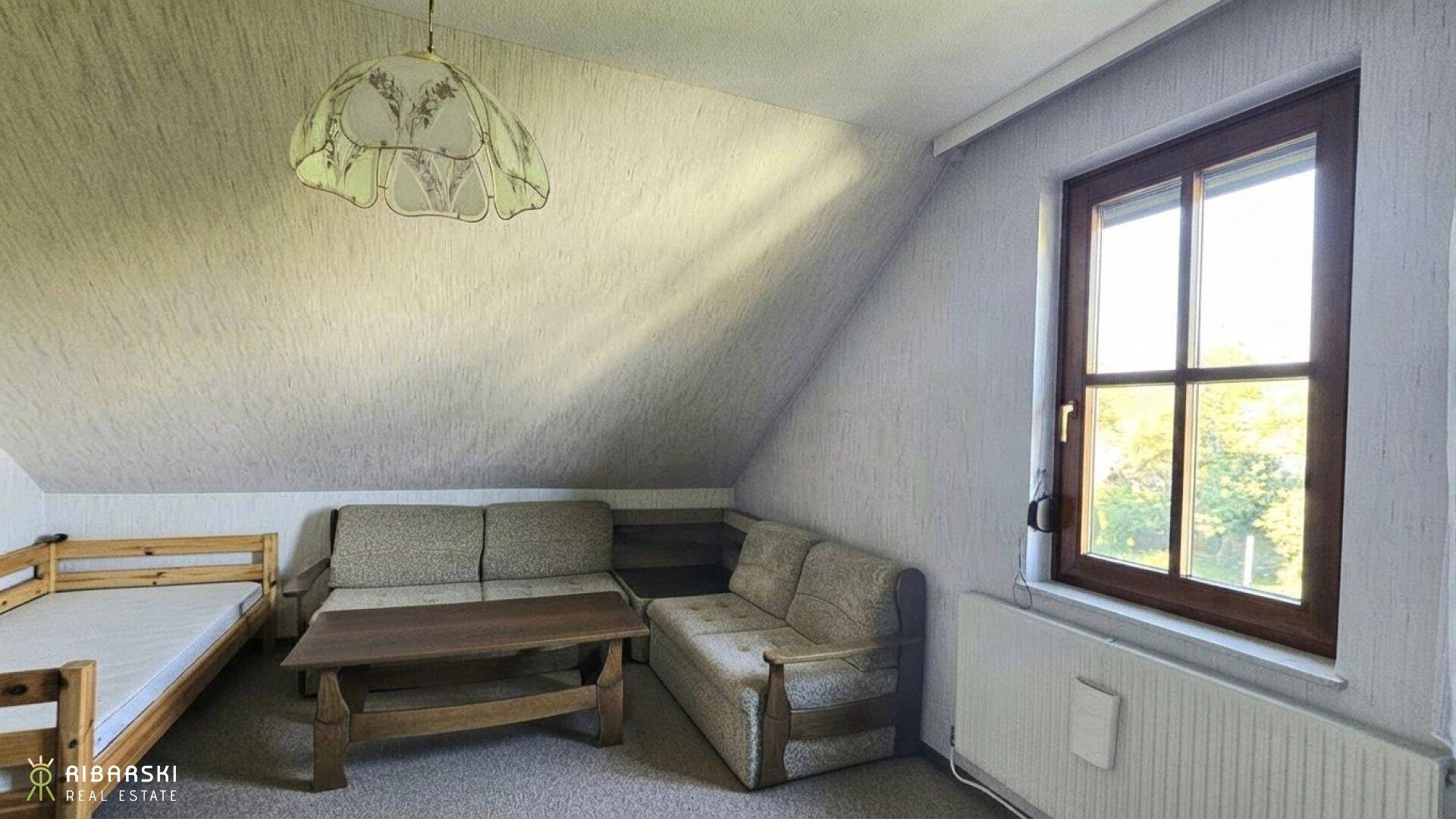 Gemütlicher Dachraum mit Schrägen, Sofa, Tisch und Bett, ideal als zusätzlicher Wohnbereich.