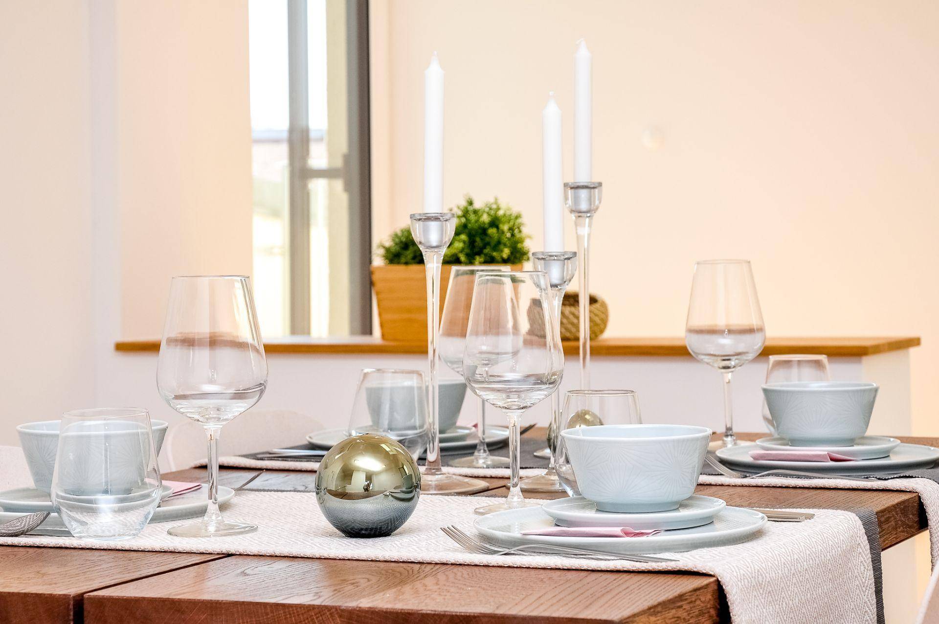 Elegant gedeckter Esstisch mit Kerzenleuchtern und Geschirr in hellen Farbtönen.