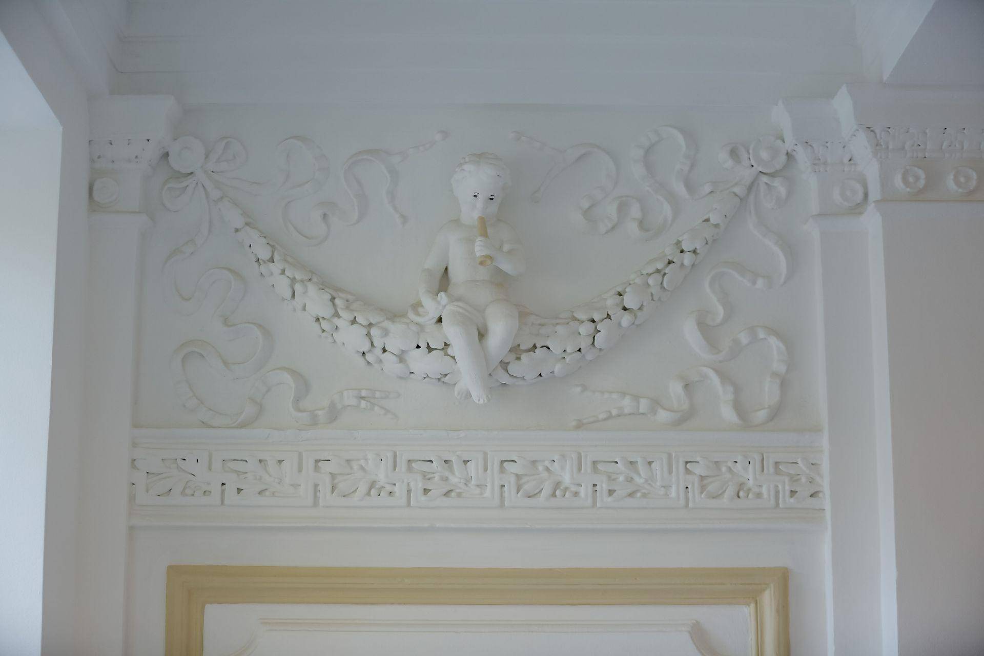 Detailaufnahme einer kunstvollen Stuckverzierung an der Wand mit einer Puttenfigur.