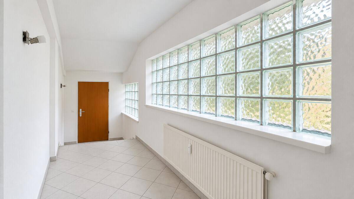 Geräumiger Flur mit Fliesenboden, Glasbausteinen und Holztür, gut beleuchtet.