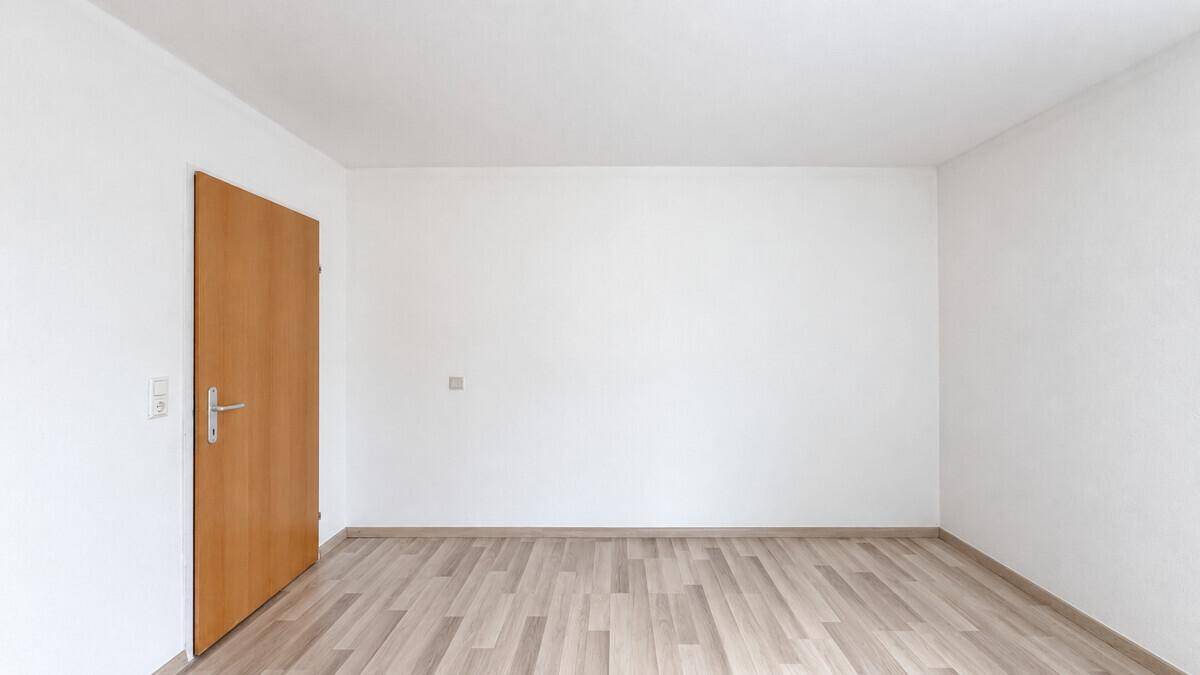 Leerer Raum mit Laminatboden und einer Holztür, bereit zur individuellen Gestaltung.
