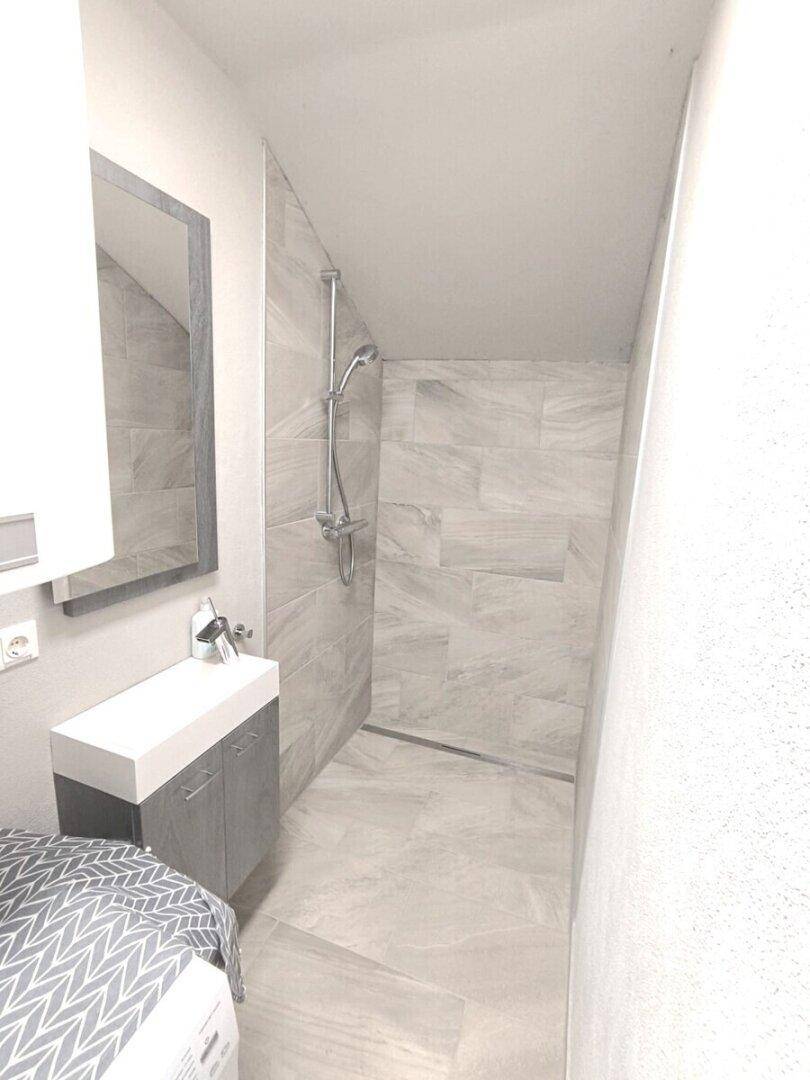 Modernes Badezimmer mit begehbarer Dusche, schrägen Wänden und hellen Fliesen.