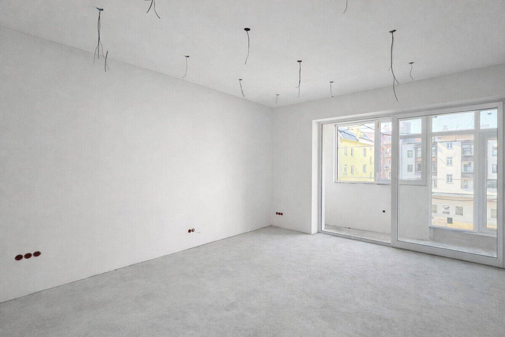 Unfertiges Zimmer mit Betonboden und vorbereiteten Elektroinstallationen, bereit für den Ausbau.
