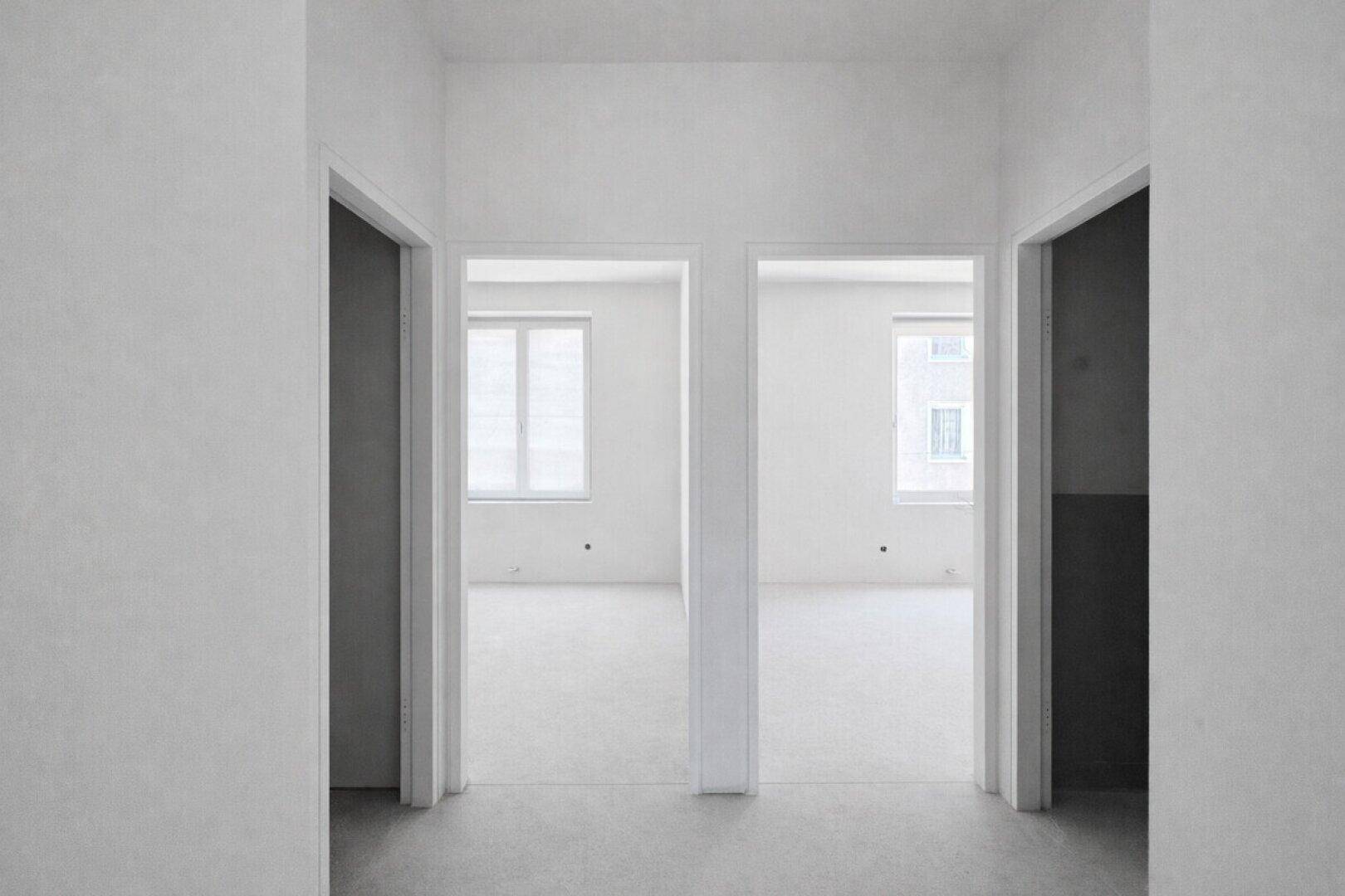 Heller Flur mit mehreren Türöffnungen zu unfertigen Räumen und Betonboden.