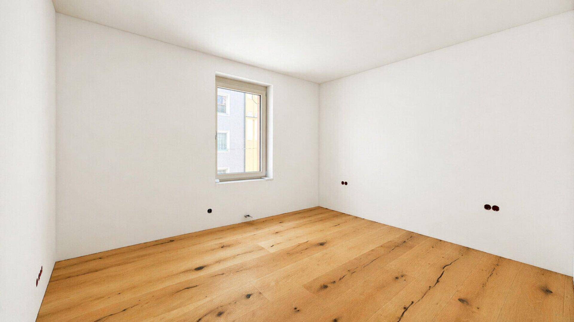 Helles, leeres Zimmer mit neuem Holzfußboden und einem Fenster, ideal für Schlaf- oder Arbeitszimmer.