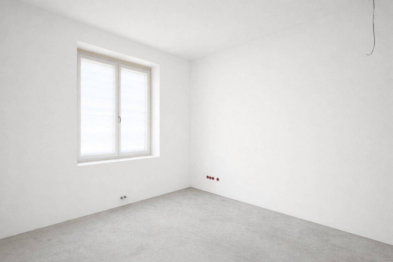 Unfertiges Zimmer mit Betonboden und großem Fenster, bereit für den Innenausbau.