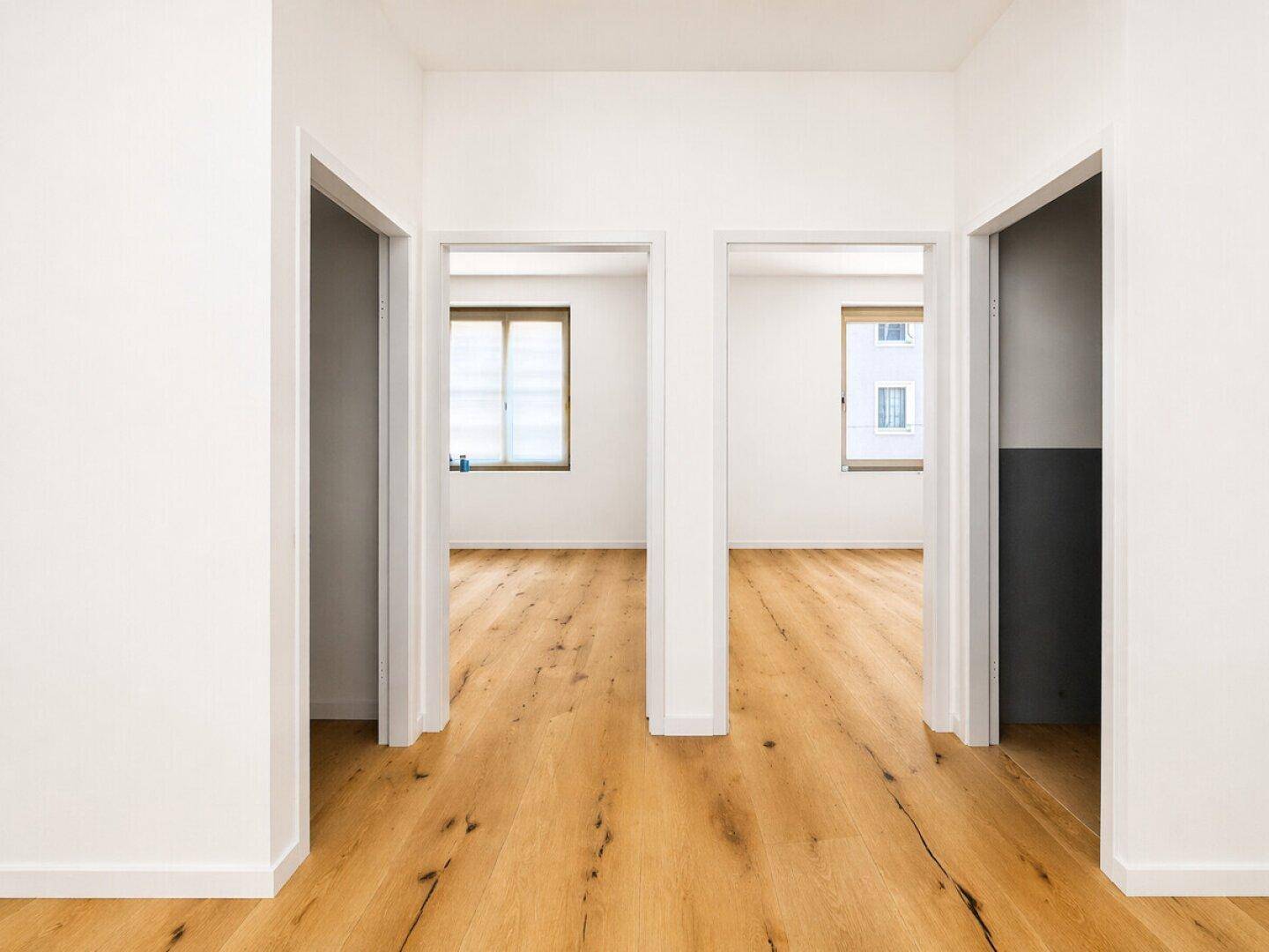 Heller Flur mit neuem Holzfußboden und Zugang zu mehreren Zimmern.