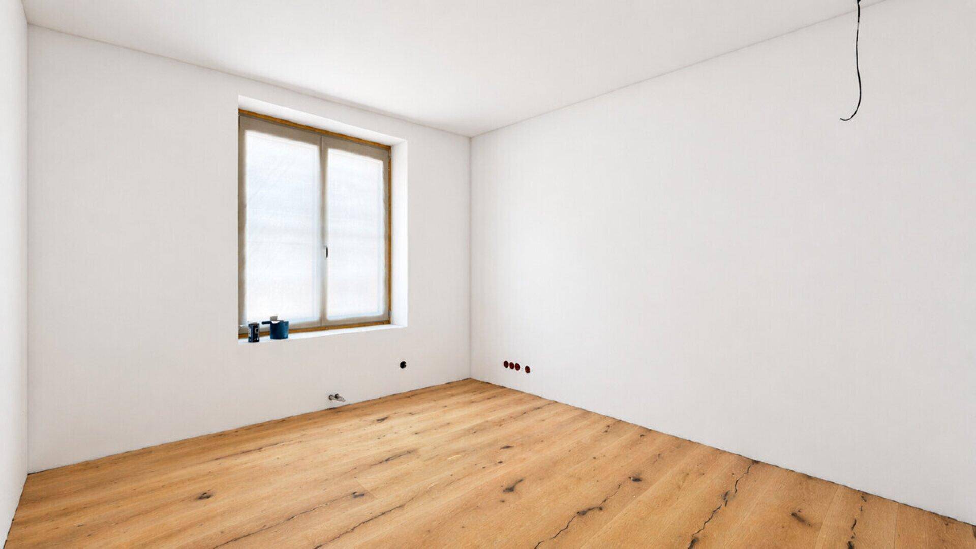 Helles, leeres Zimmer mit neuem Holzfußboden und großem Fenster, ideal für Schlaf- oder Kinderzimmer.