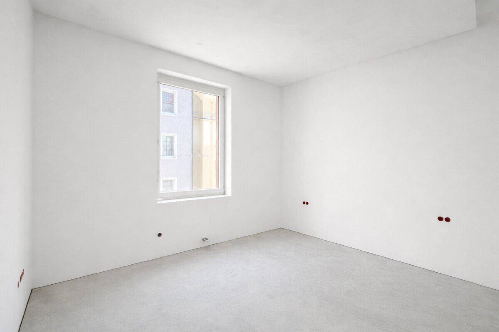 Leeres Zimmer mit Betonboden und einem Fenster, bereit für die individuelle Gestaltung.