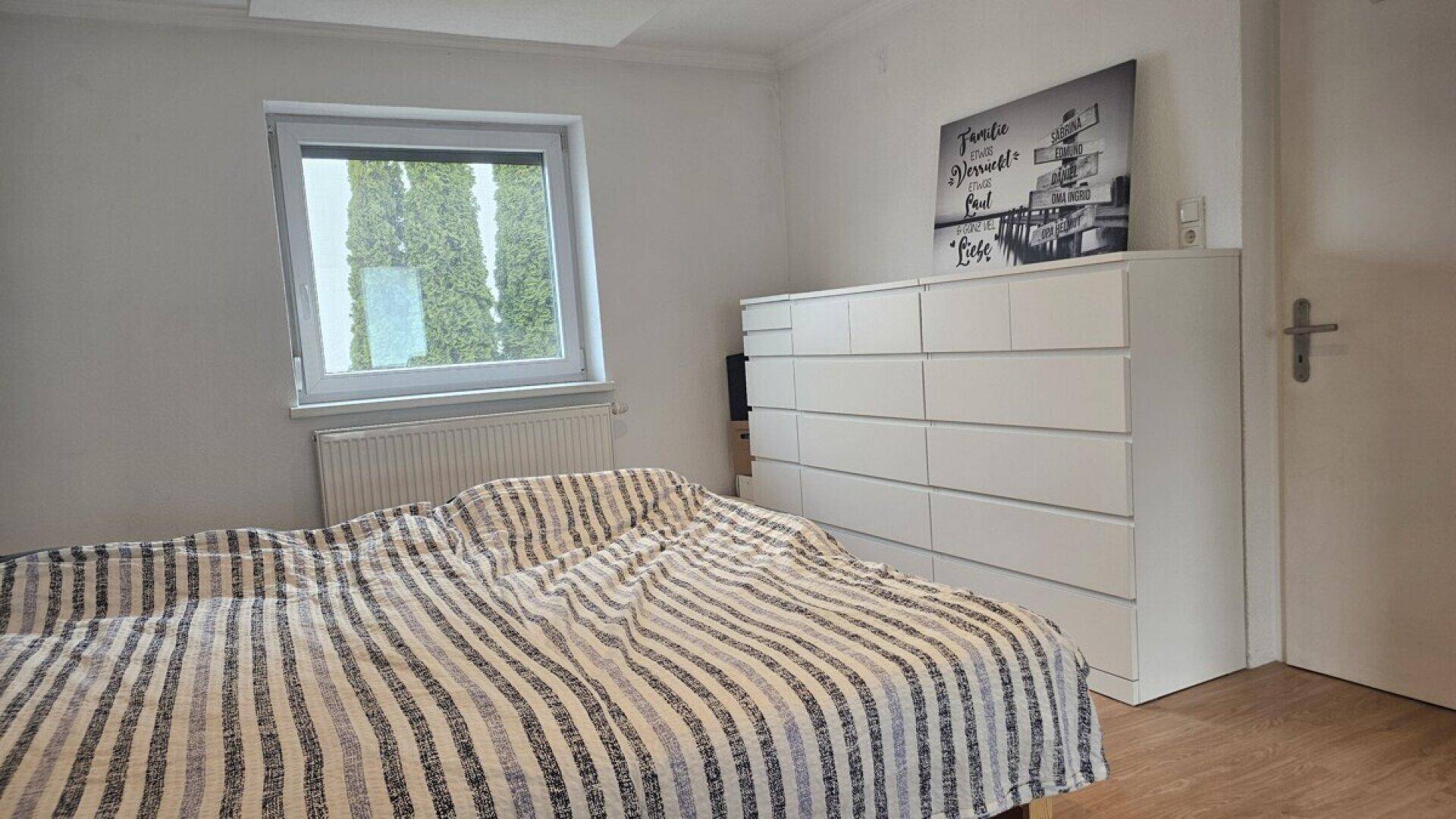Gemütliches Schlafzimmer mit Doppelbett, weißer Kommode und Blick ins Grüne.