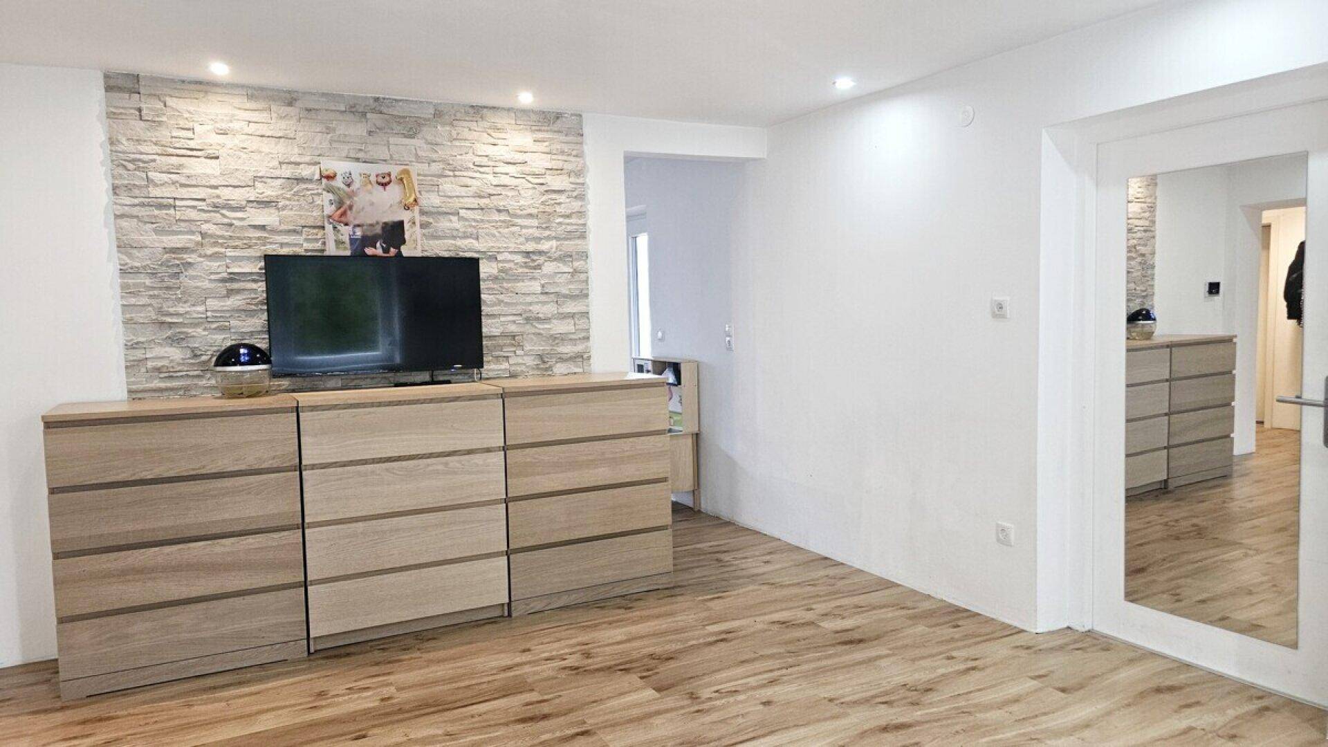 Geräumiger Wohnraum mit dekorativer Steinwand, Holzmöbeln und viel Tageslicht.