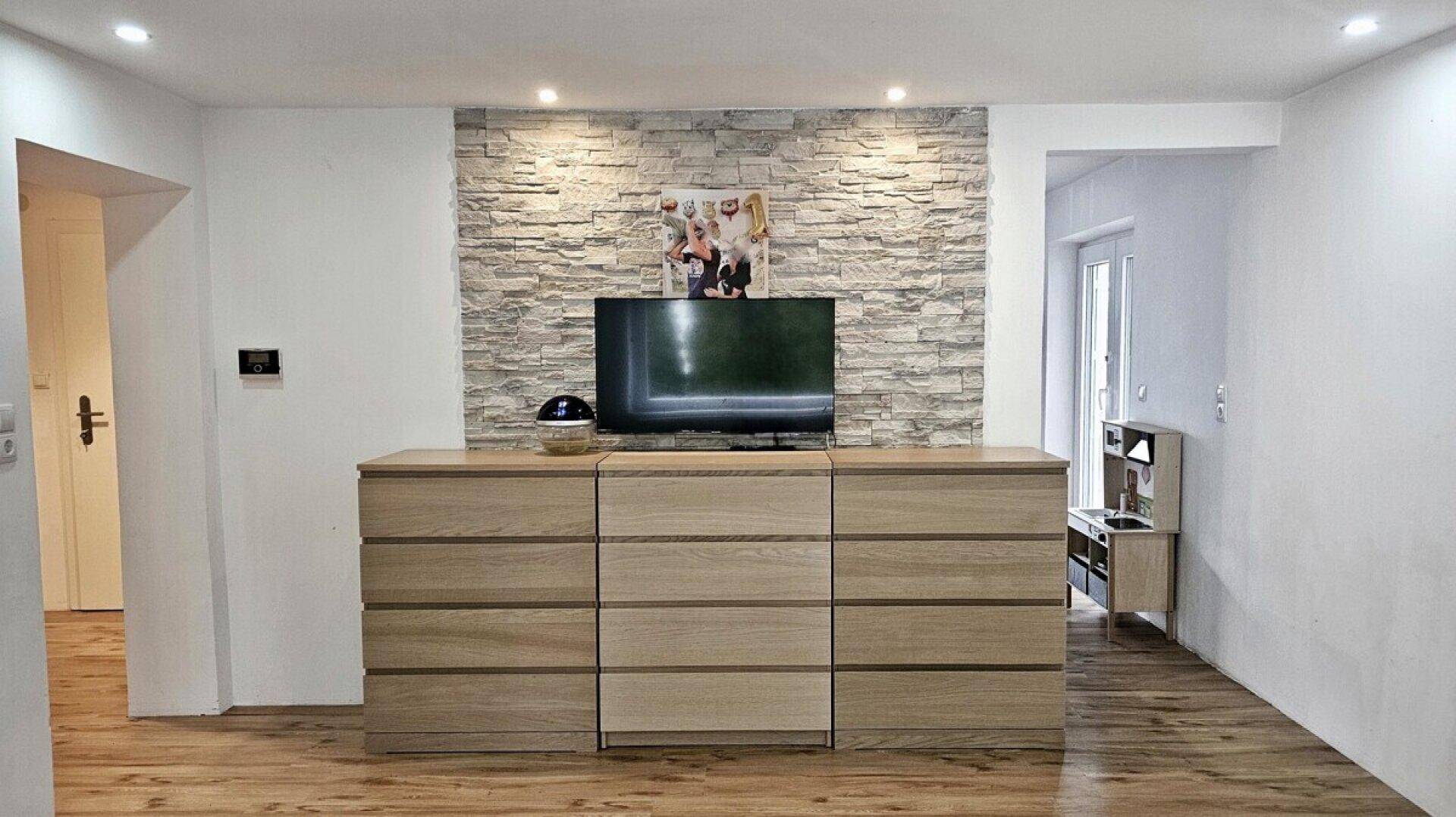 Detailansicht der Steinwand im Wohnzimmer mit Fernseher und einem langen Holzschrank.