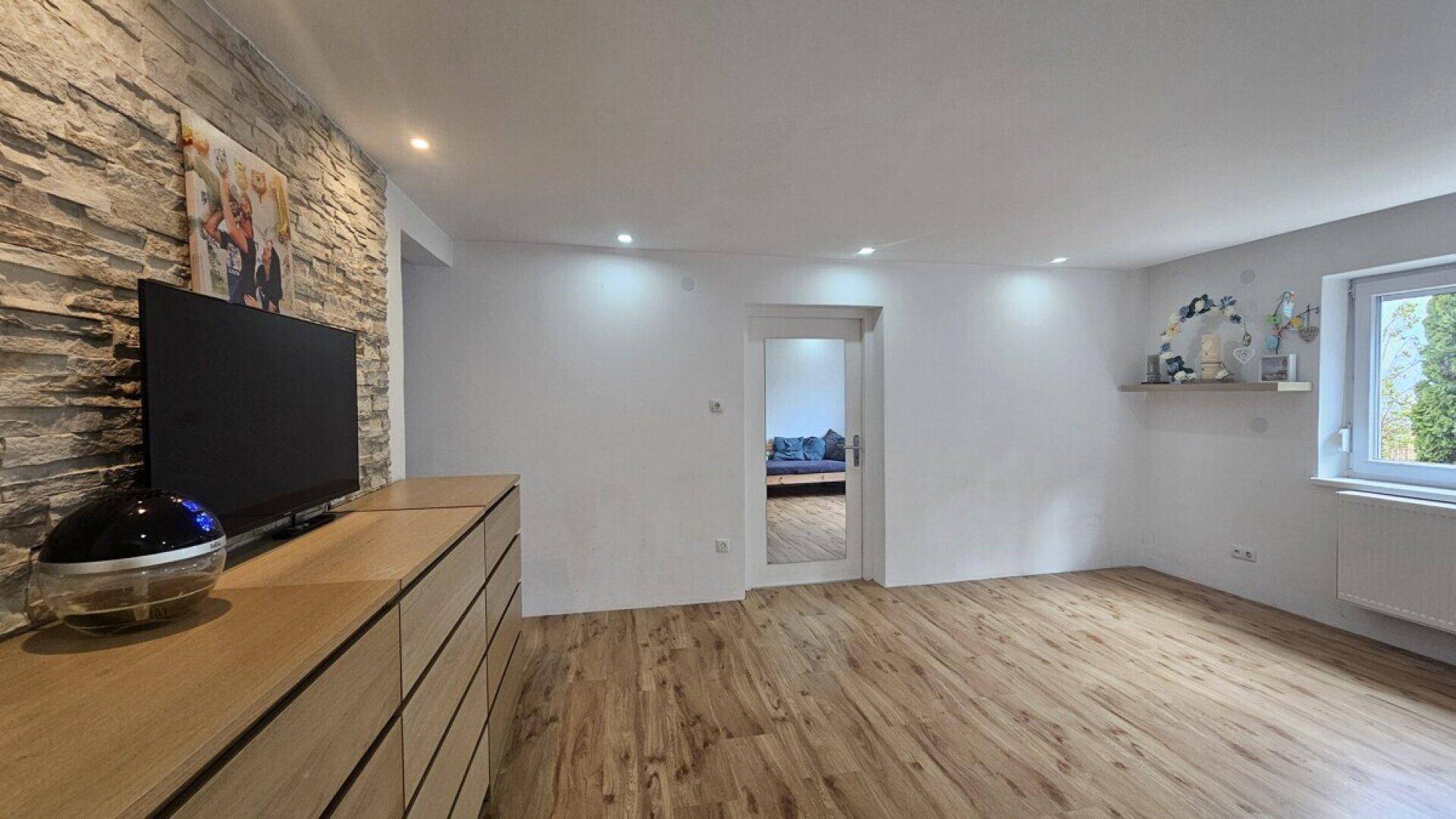 Heller Wohnbereich mit Laminatboden, einer Steinwand und einem modernen Sideboard.