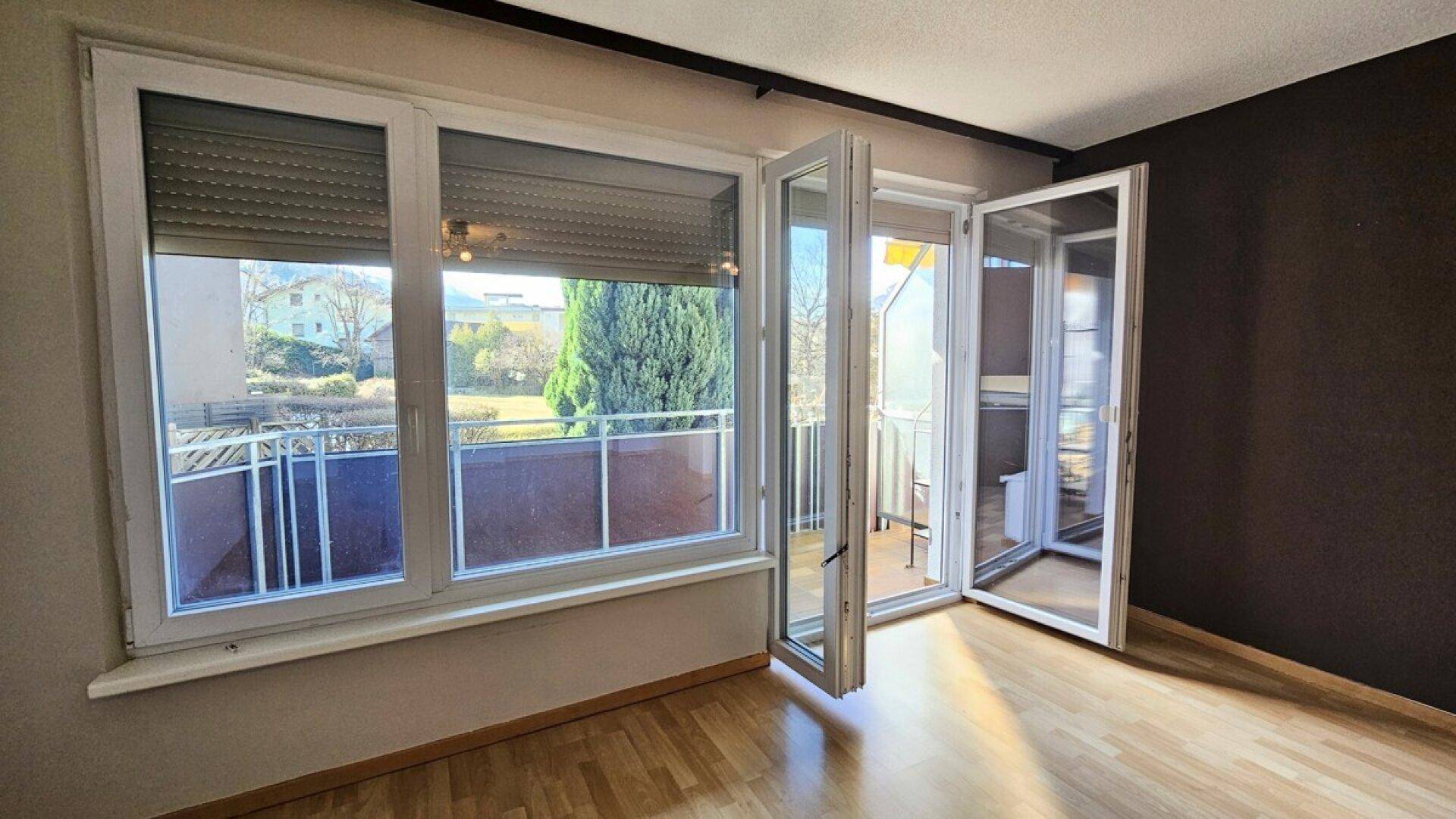 Helles Wohnzimmer mit Holzboden und Zugang zu einem Balkon mit Blick ins Grüne.