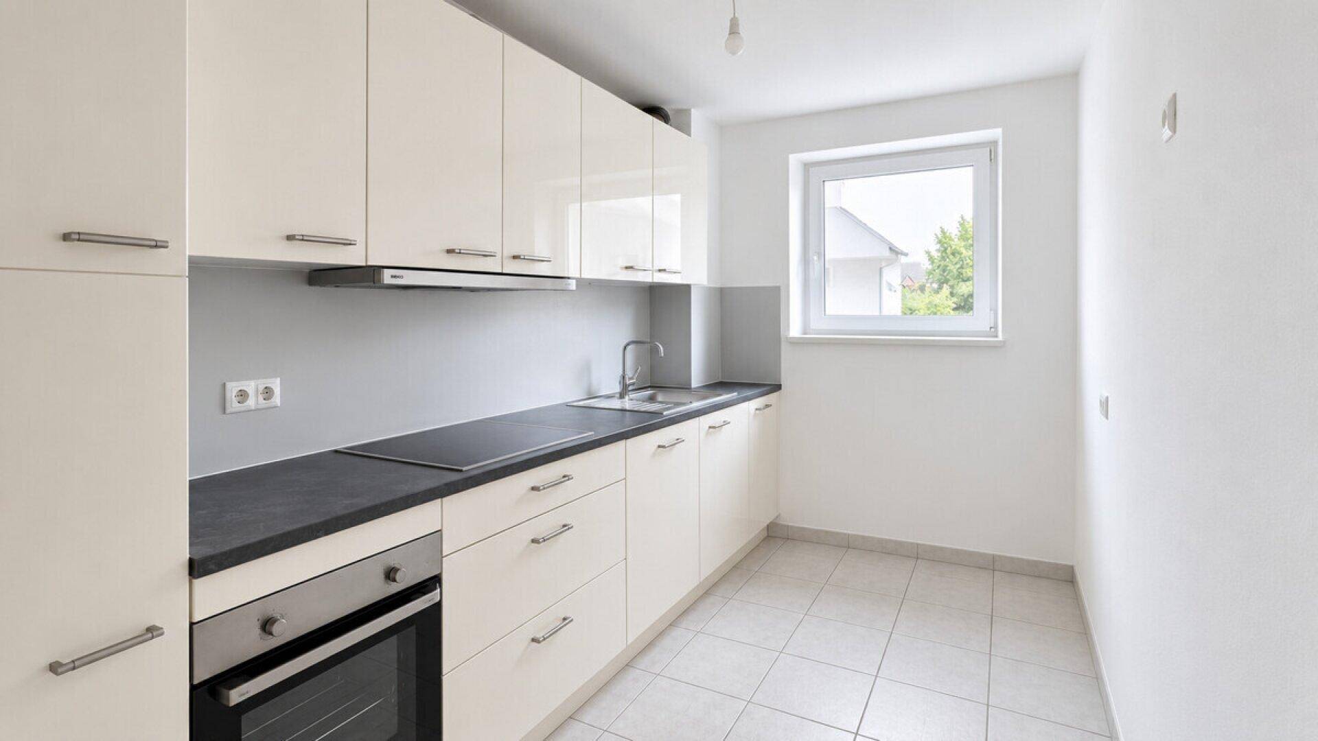 Moderne Einbauküche mit weißen Hochglanzfronten, dunkler Arbeitsplatte und Fenster.