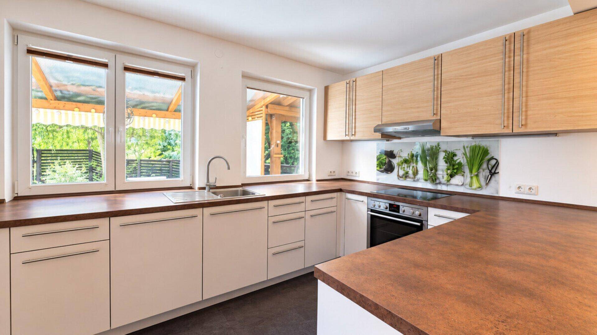Helle Küche mit Holzschränken, großem Fenster und Arbeitsplatte, die viel Platz bietet.