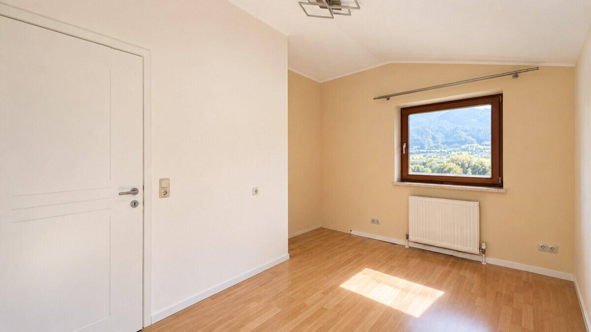 Helles Schlafzimmer mit Parkettboden, Fenster und Blick auf die umliegende Landschaft.