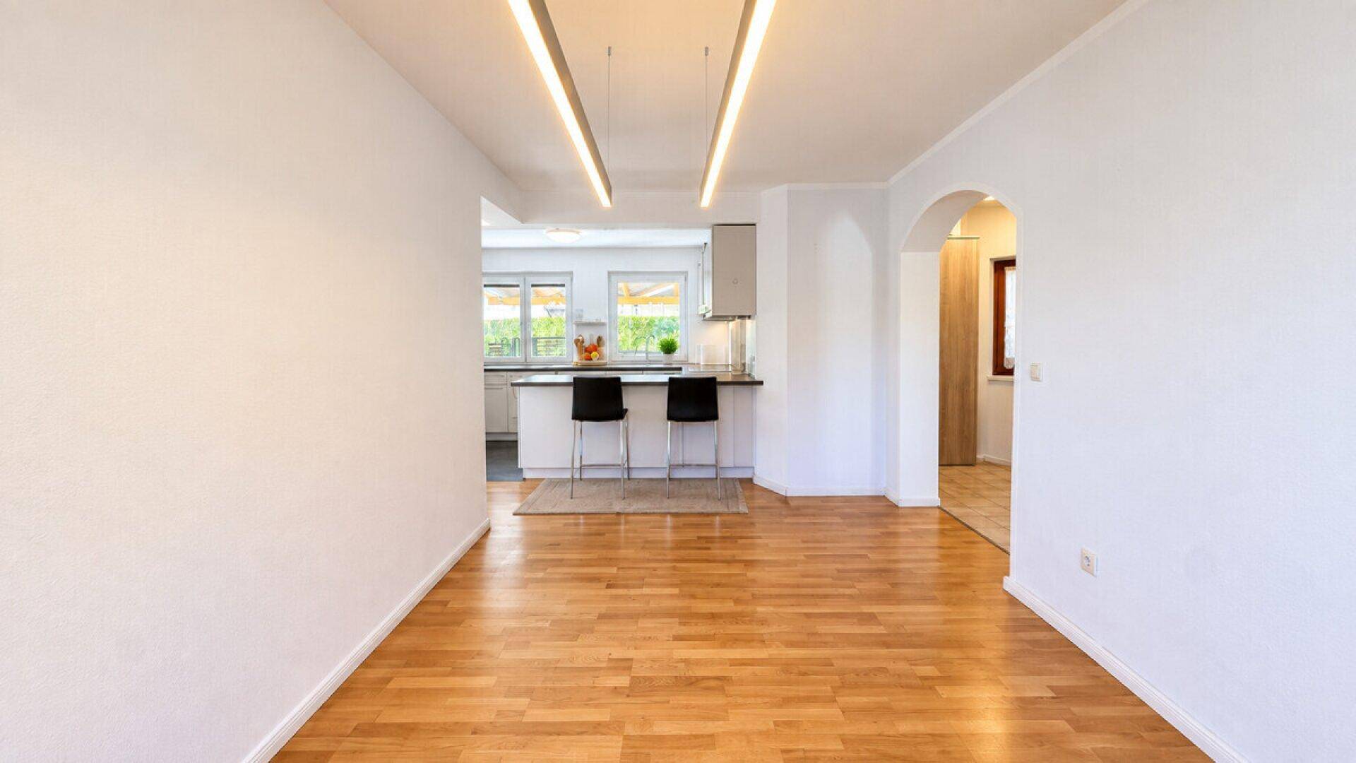 Geräumiger Wohnbereich mit hellem Parkettboden und offenem Übergang zur Küche.