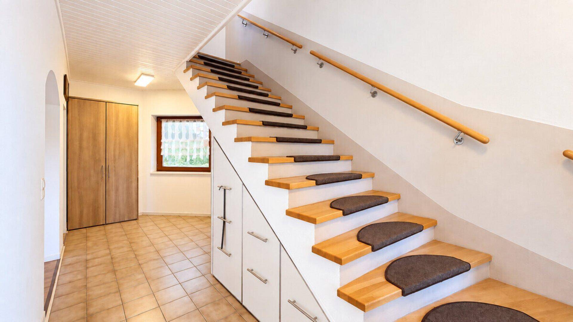 Heller Flur mit Holztreppe, Stauraum unter der Treppe und Fliesenboden.