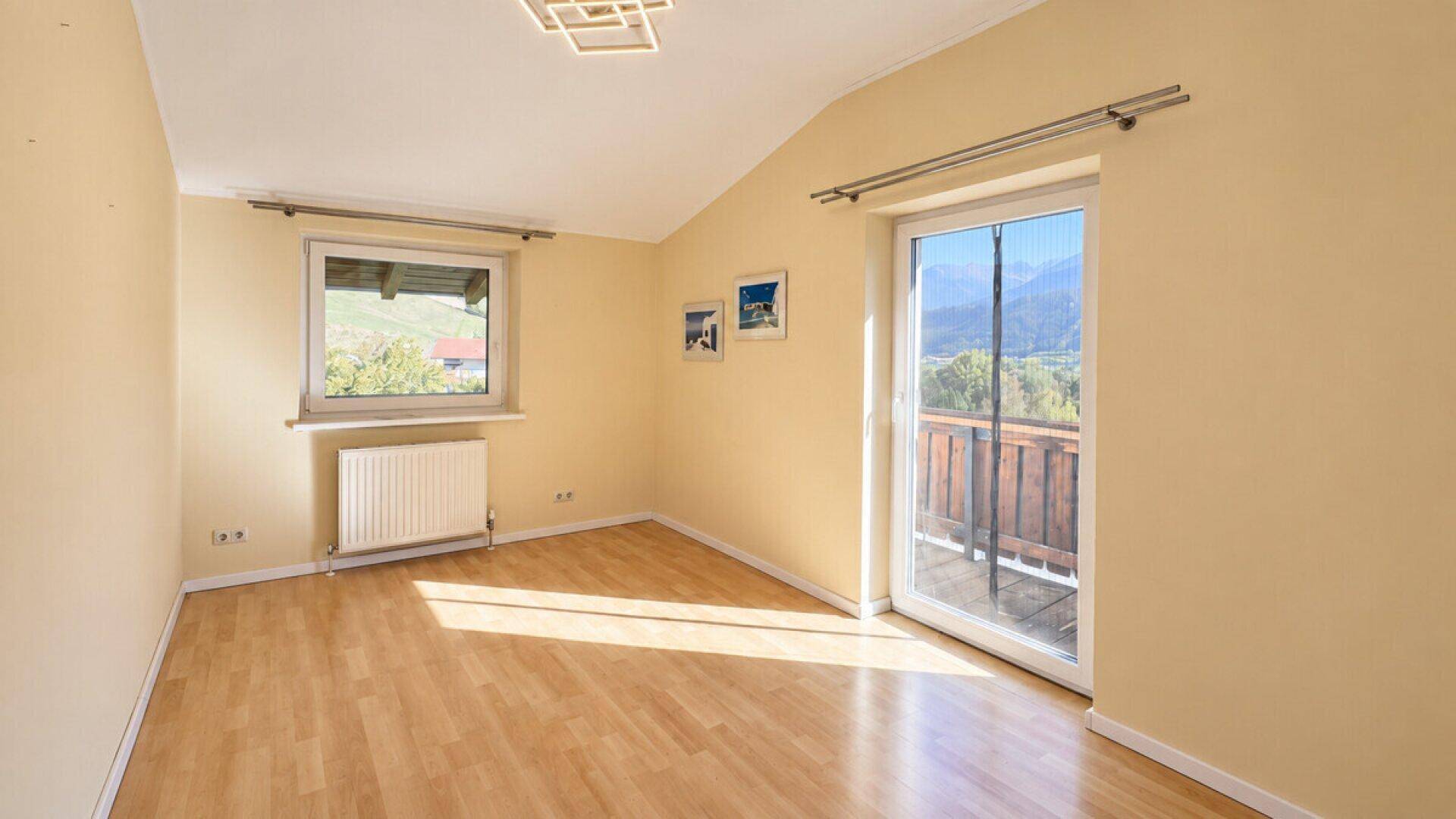 Schlafzimmer mit Parkettboden, Balkonzugang und weitem Blick auf die Berge.