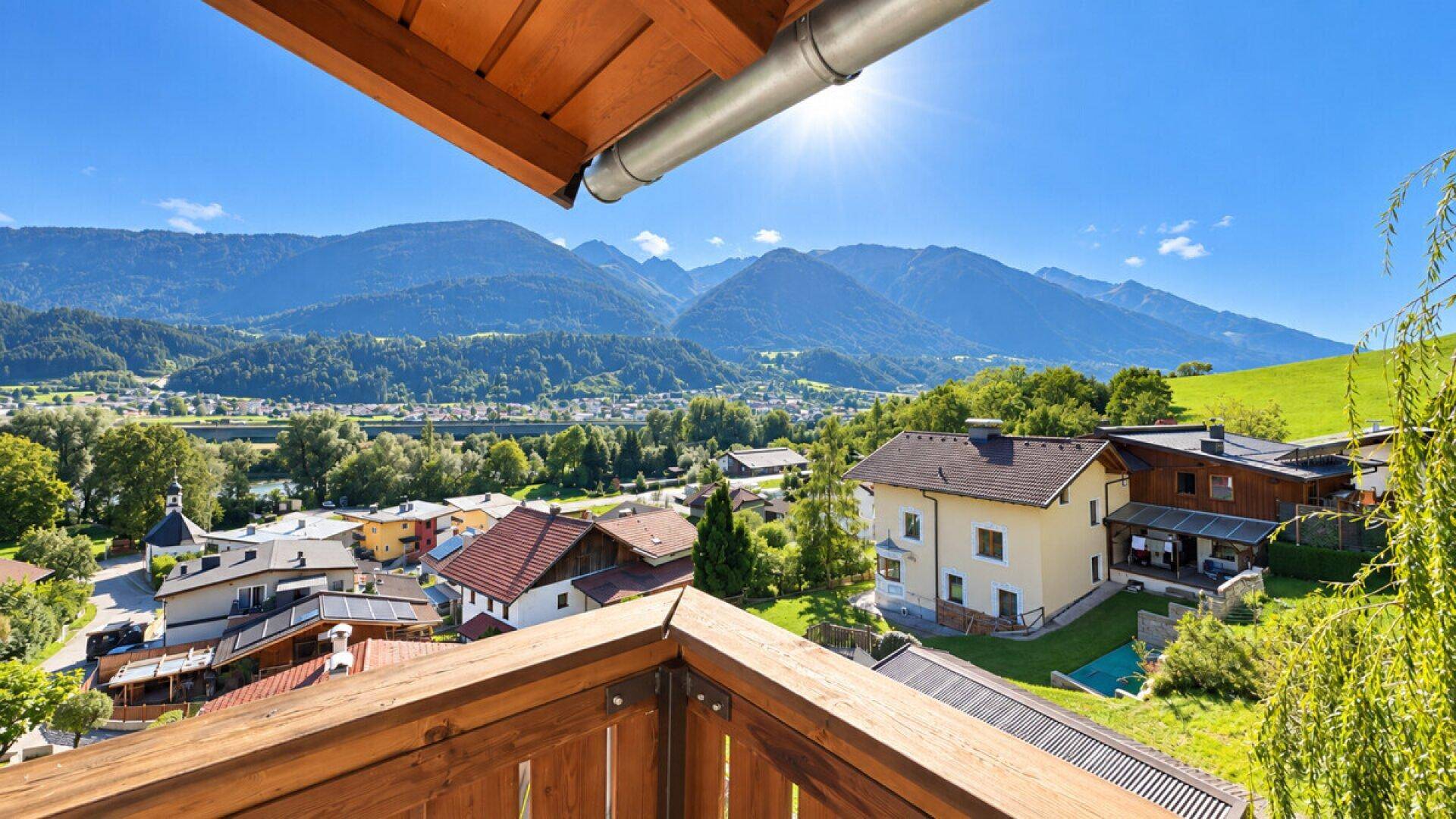 Sonniger Balkon mit Holzelementen und Panoramablick auf die Berge und das Tal.