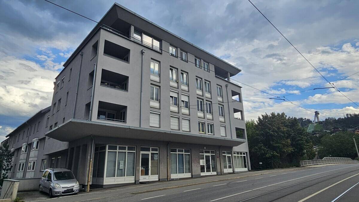 Modernes Mehrfamilienhaus mit grauer Fassade und Geschäften im Erdgeschoss an einer Straße.