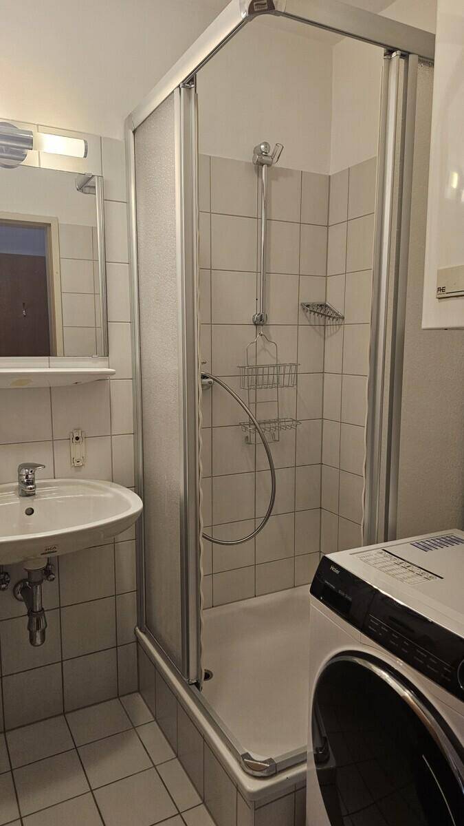 Badezimmer mit Duschkabine, Waschbecken und Waschmaschine.