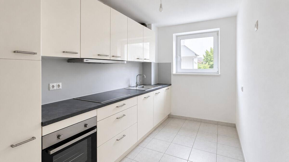 Moderne, helle Küche mit weißen Hochglanzschränken, dunkler Arbeitsplatte und Fenster.