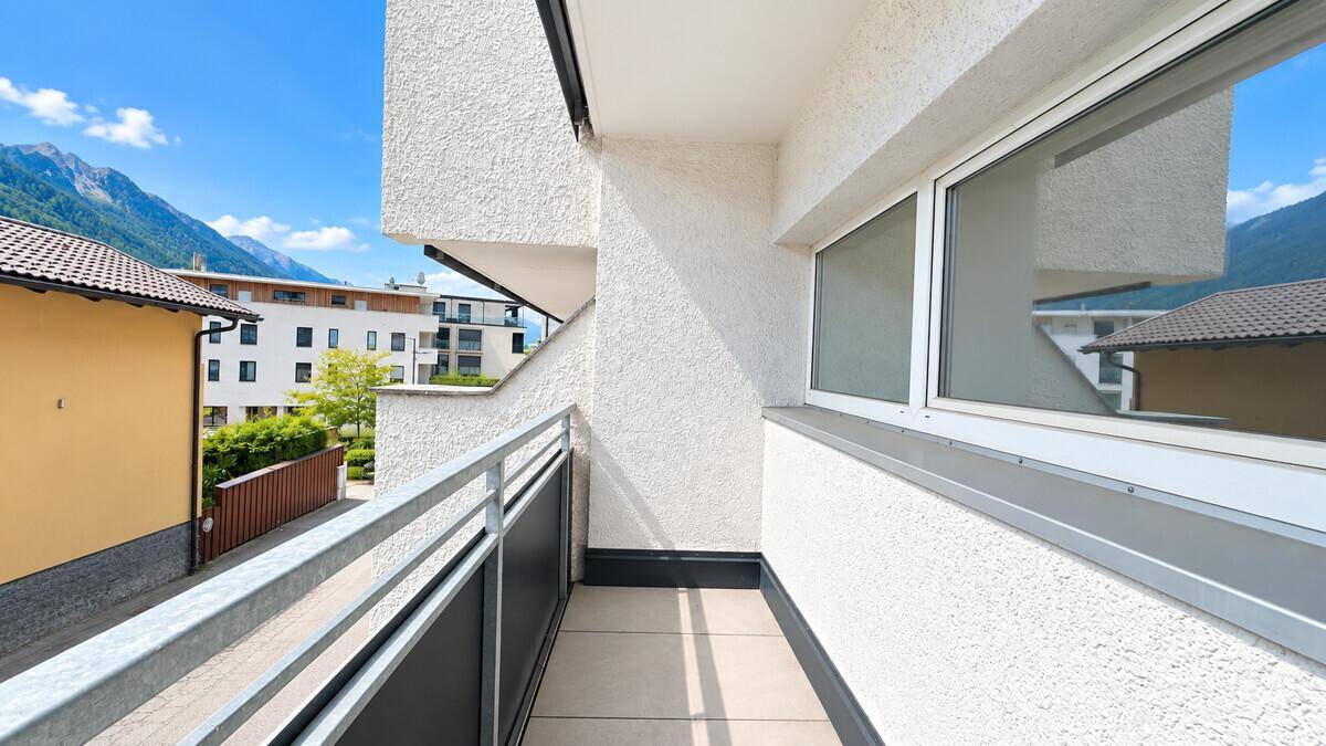 Moderner Balkon mit Metallgeländer und Blick auf die umliegenden Berge und Gebäude.