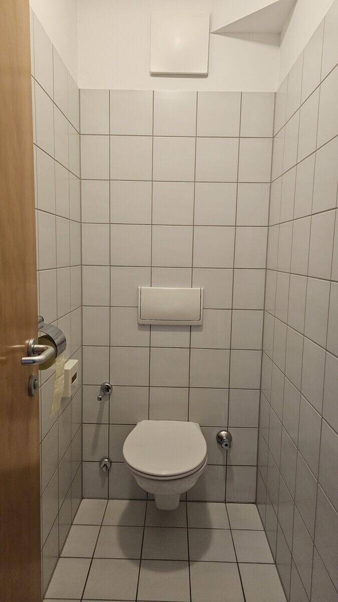 Separates WC mit weißen Fliesen und wandmontierter Toilette.