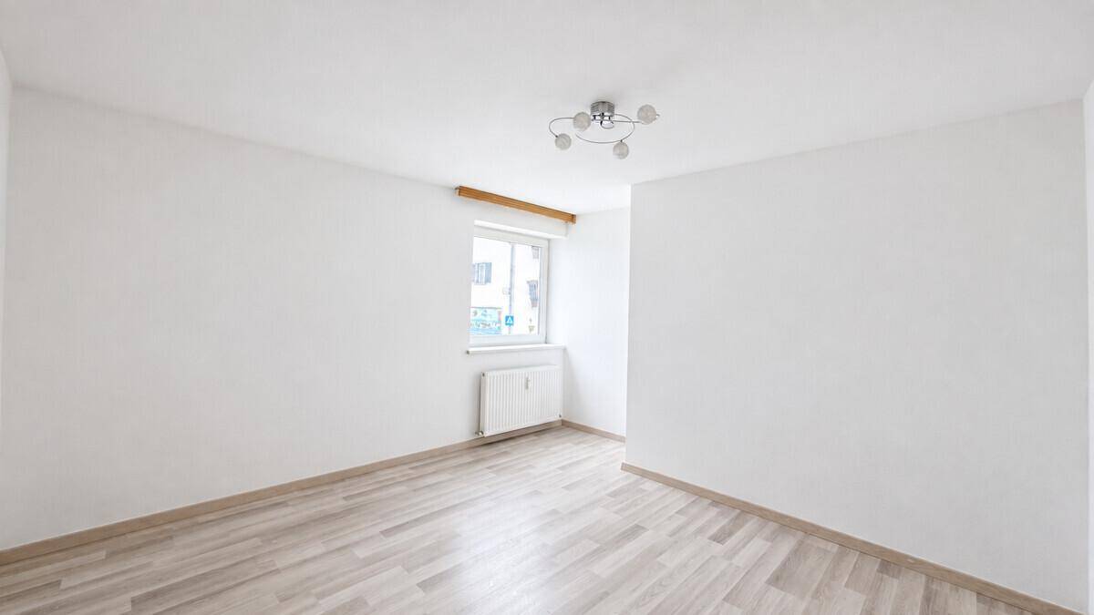 Helles, leeres Zimmer mit Laminatboden und einem Fenster, ideal als Schlafzimmer.