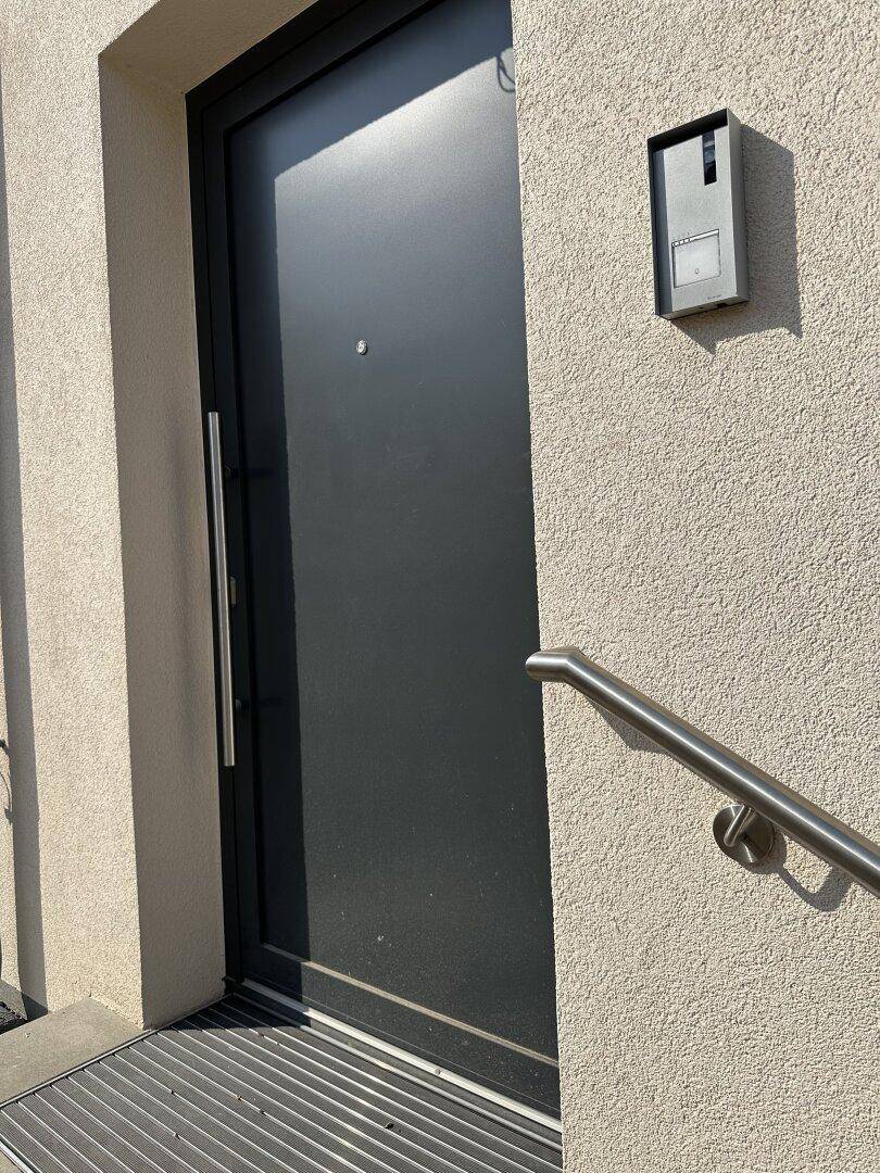 Moderne Eingangstür in dunklem Anthrazit mit Edelstahlgriff und Gegensprechanlage.
