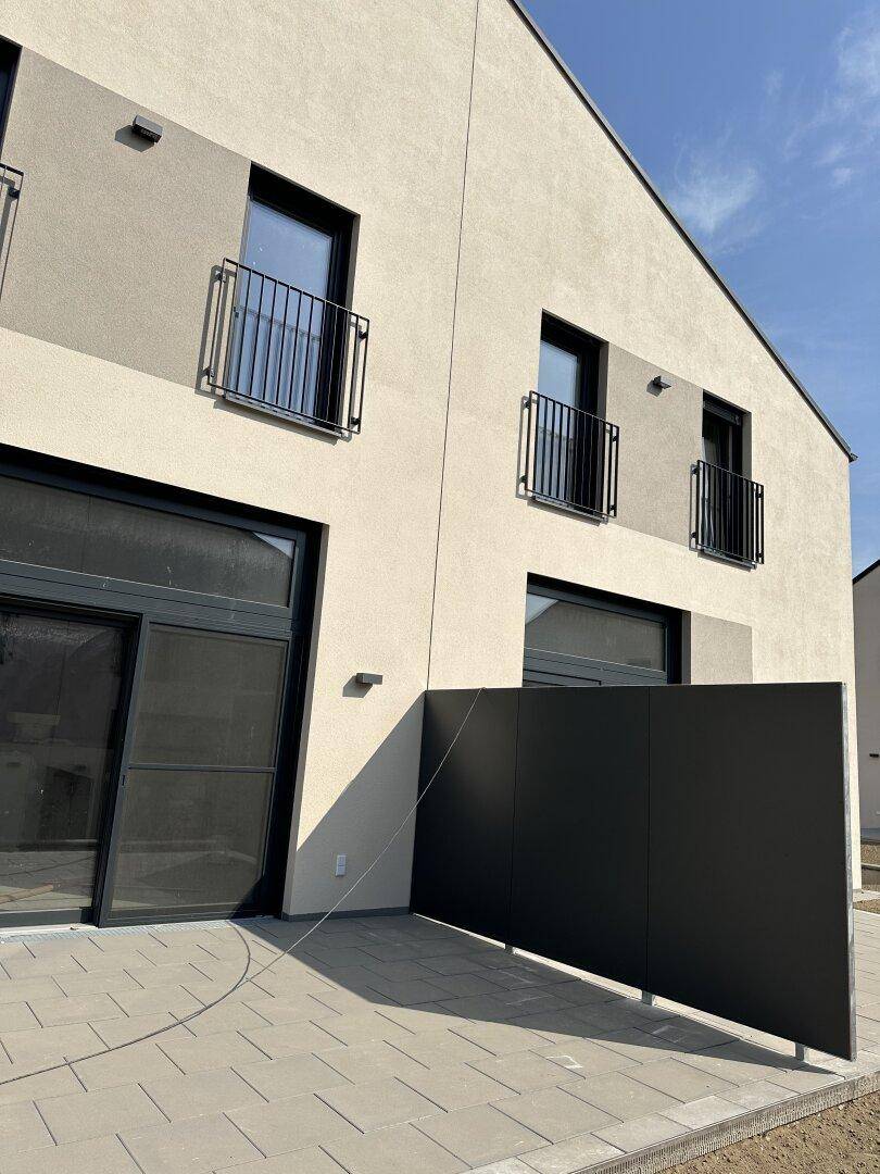 Nahaufnahme der modernen Fassade eines Reihenhauses mit Terrasse und Balkonen unter blauem Himmel.