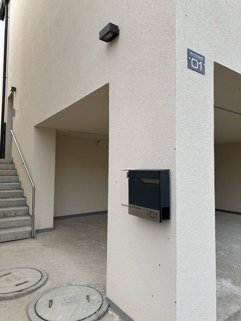 Moderner Eingangsbereich eines Reihenhauses mit Treppe, stilvollem Briefkasten und Hausnummer.